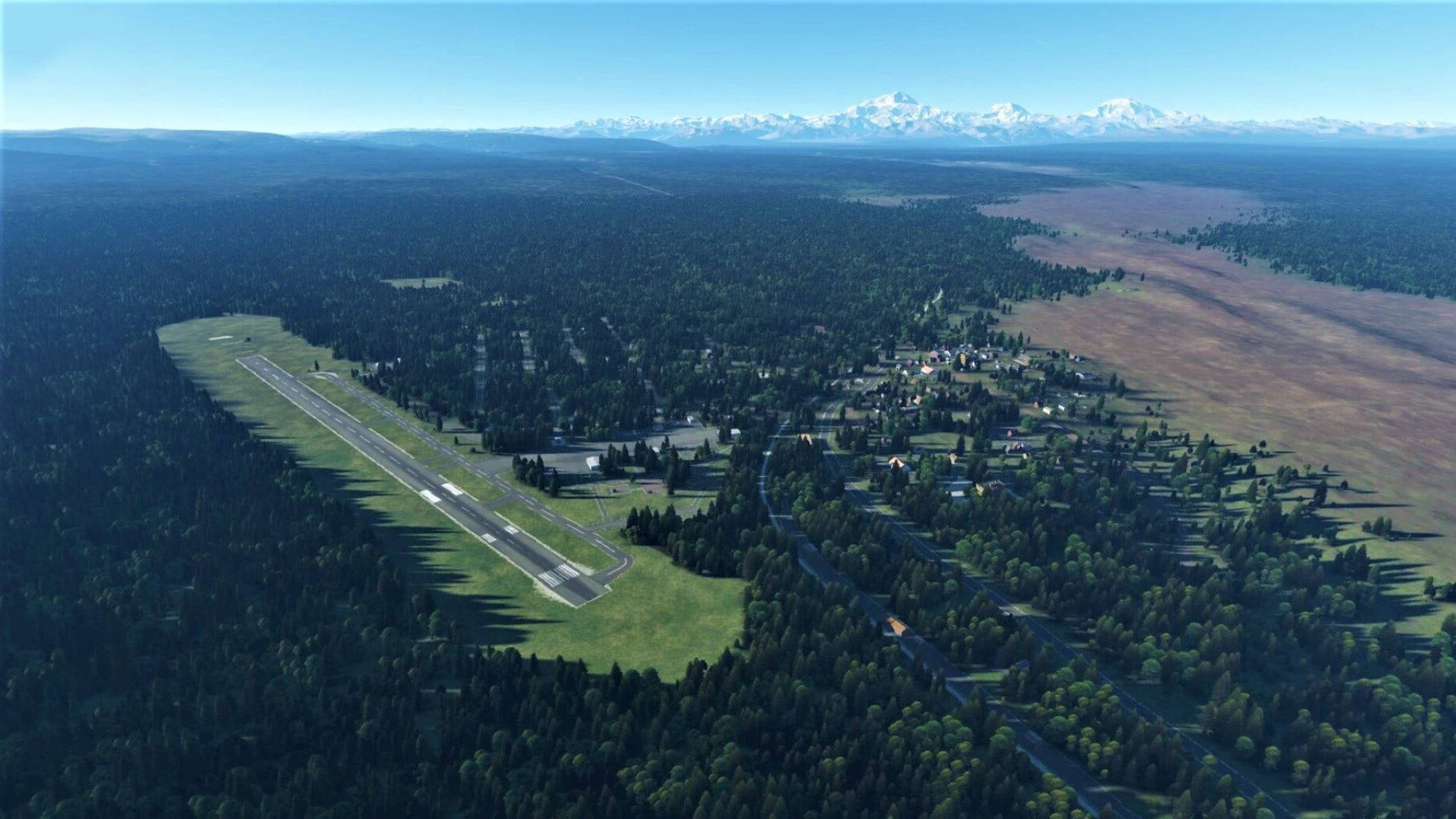 Runway 桌布 壁紙 — 從高空俯瞰一個坐落在森林山谷中的小型機場，遠方是白雪覆蓋的山峰，天空清澈湛藍。