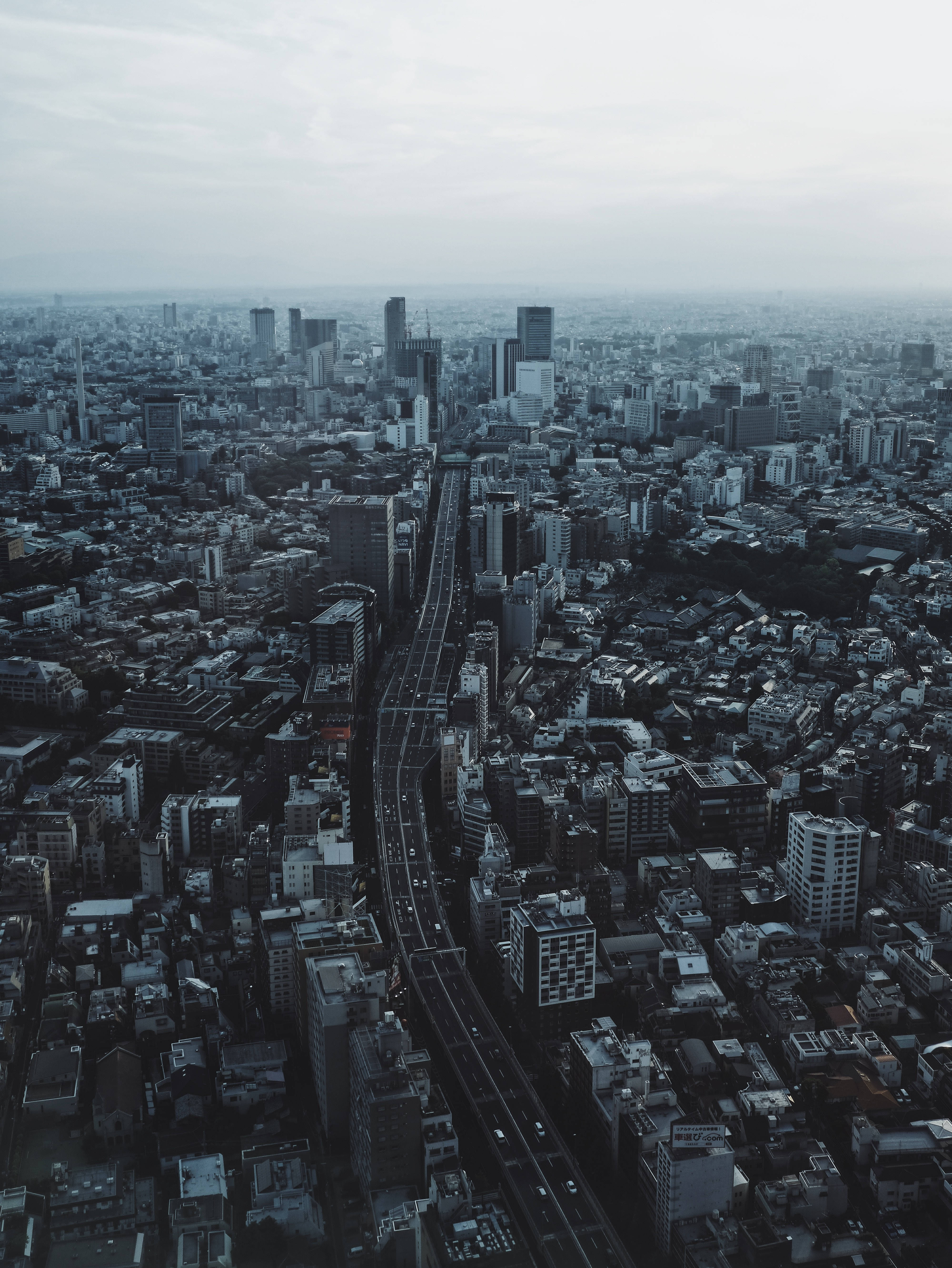 東京 桌布 壁紙 — 從高空俯瞰一個廣闊的城市，建築密集，一條中央高速公路穿過城市，天空多雲。