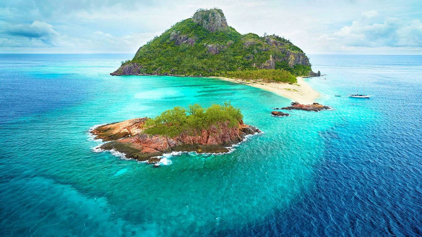 Fiji 桌布 壁紙 — 從高空俯瞰一個鬱鬱蔥蔥的綠色島嶼，擁有沙灘，四周環繞著充滿活力的碧綠海水，遠處有一艘小船。