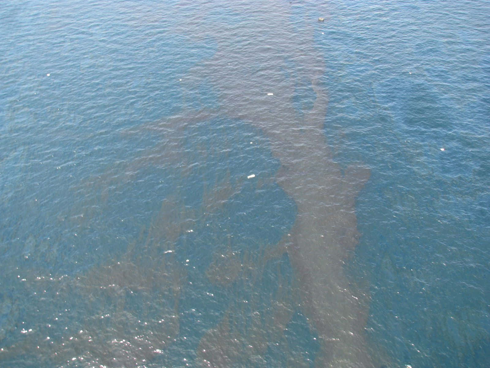 Ocean Water 桌布 壁紙 — 從高空俯瞰一大片深色油污在波光粼粼的藍色海面上擴散。