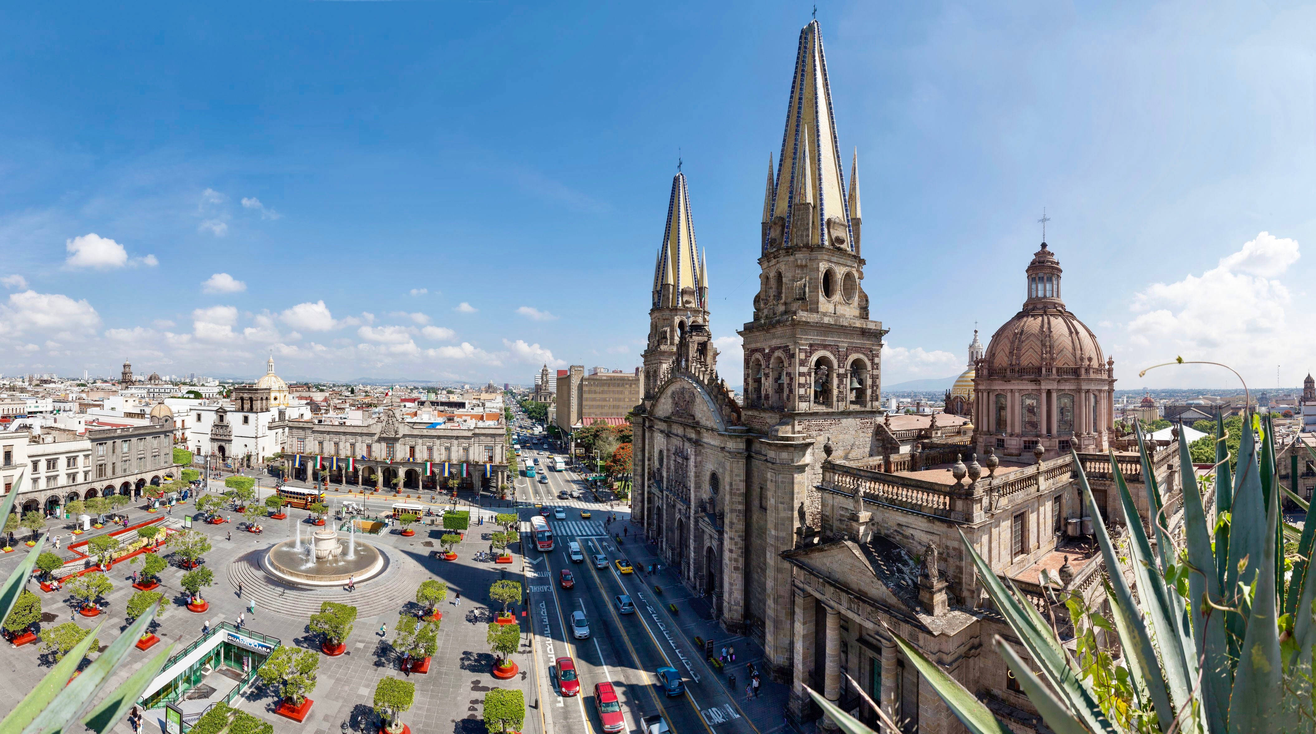 Guadalajara 桌布 壁紙 — 從高空俯瞰一座宏偉的大教堂，其雙塔在晴朗的藍天下主宰著繁忙的城市廣場。