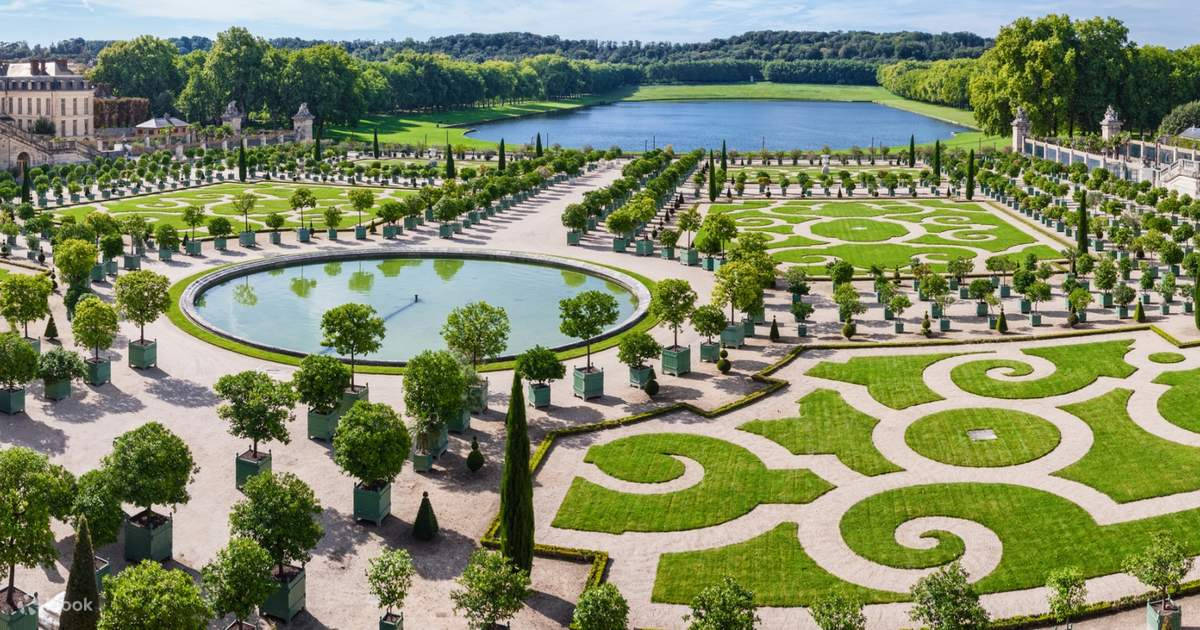 Beautiful Landscape 桌布 壁紙 — 從高空俯瞰一座宏偉的正式花園，擁有對稱的綠色草坪、幾何圖案、圓形池塘和遠處的湖泊，周圍環繞著茂密的樹木，陽光明媚。
