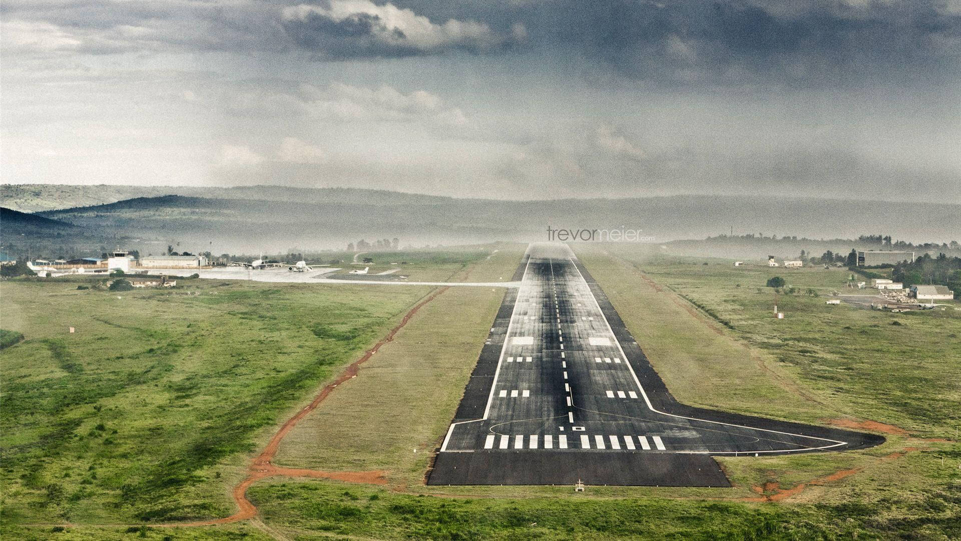 Runway 桌布 壁紙 — 從高空俯瞰一條長長的機場跑道，穿過霧氣瀰漫的綠色田野，天空多雲。