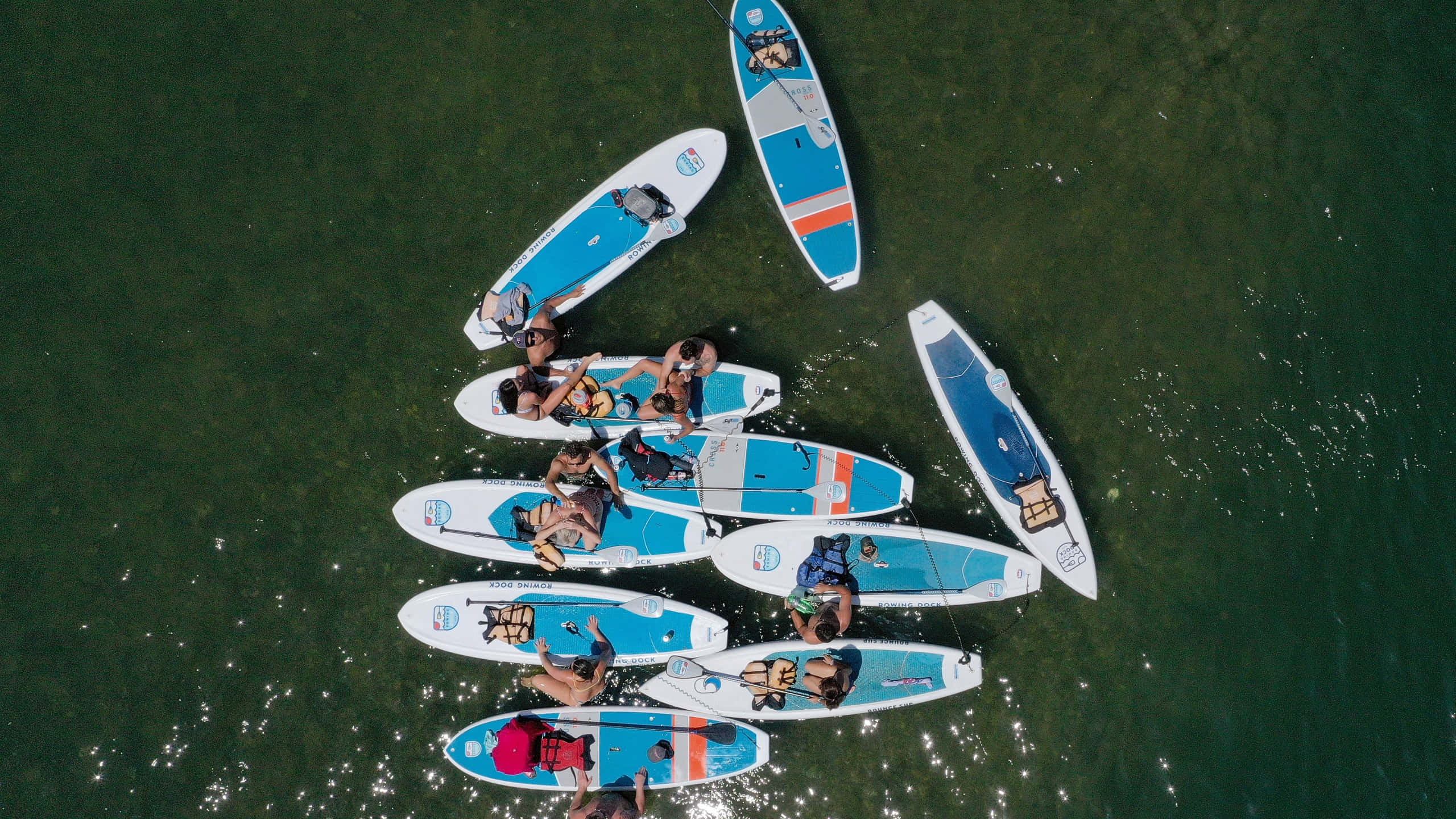 Paddleboarding 桌布 壁紙 — 從高空俯瞰一群人在平靜的綠色水面上排列成圓形的槳板。