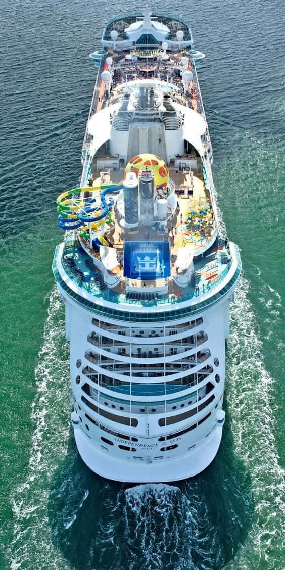 Cruise 桌布 壁紙 — 從高空俯瞰一艘巨型郵輪在碧綠色的海面上破浪前行，甲板上的色彩繽紛滑水道和泳池清晰可見。