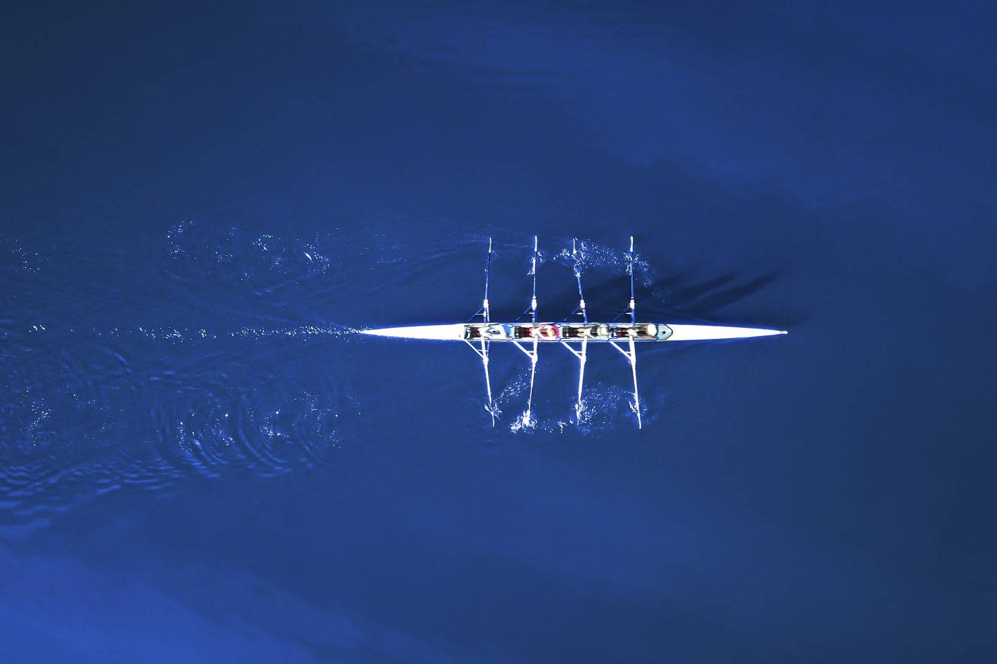 Rowing 桌布 壁紙 — 從高空俯瞰一艘流線型白色賽艇劃破深藍色水面，運動員動作同步。