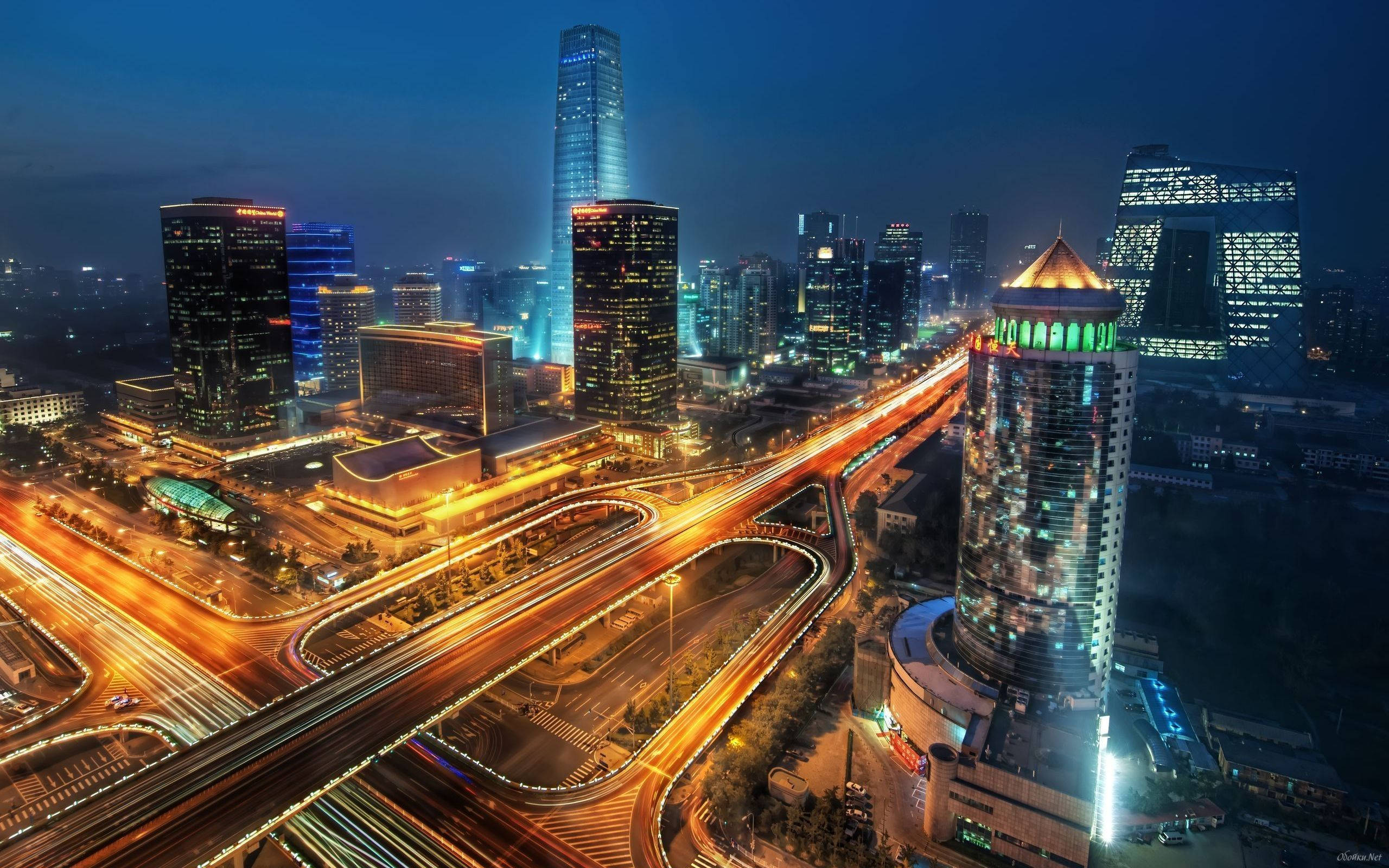 圖片 桌布 壁紙 — 從高空俯瞰充滿活力的城市夜景，閃爍的摩天大樓和流動的交通燈光照亮蜿蜒的高速公路。