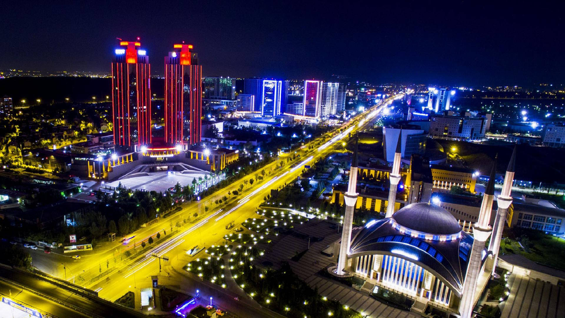 Ankara 桌布 壁紙 — 從高空俯瞰充滿活力的城市景觀，閃爍的摩天大樓和一座宏偉的、帶有宣禮塔的燈光清真寺。