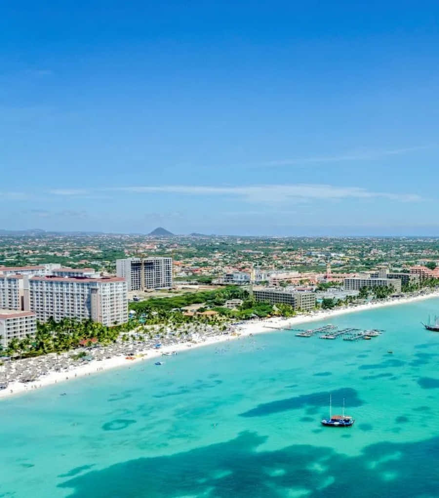 Aruba 桌布 壁紙 — 從高空俯瞰充滿活力的熱帶海灘，碧綠的海水、白色的沙灘、度假村和遠處的山脈，在清澈的藍天下。