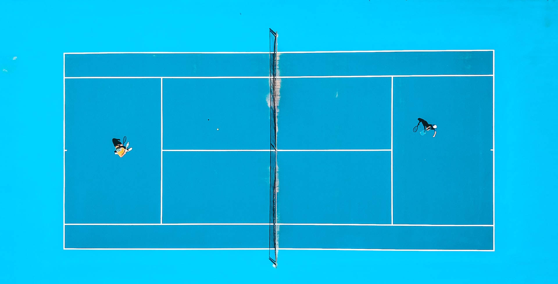 Athletic 桌布 壁紙 — 從高空俯瞰兩名網球運動員在充滿活力的藍色球場上比賽，球場上有清晰的白色線條。