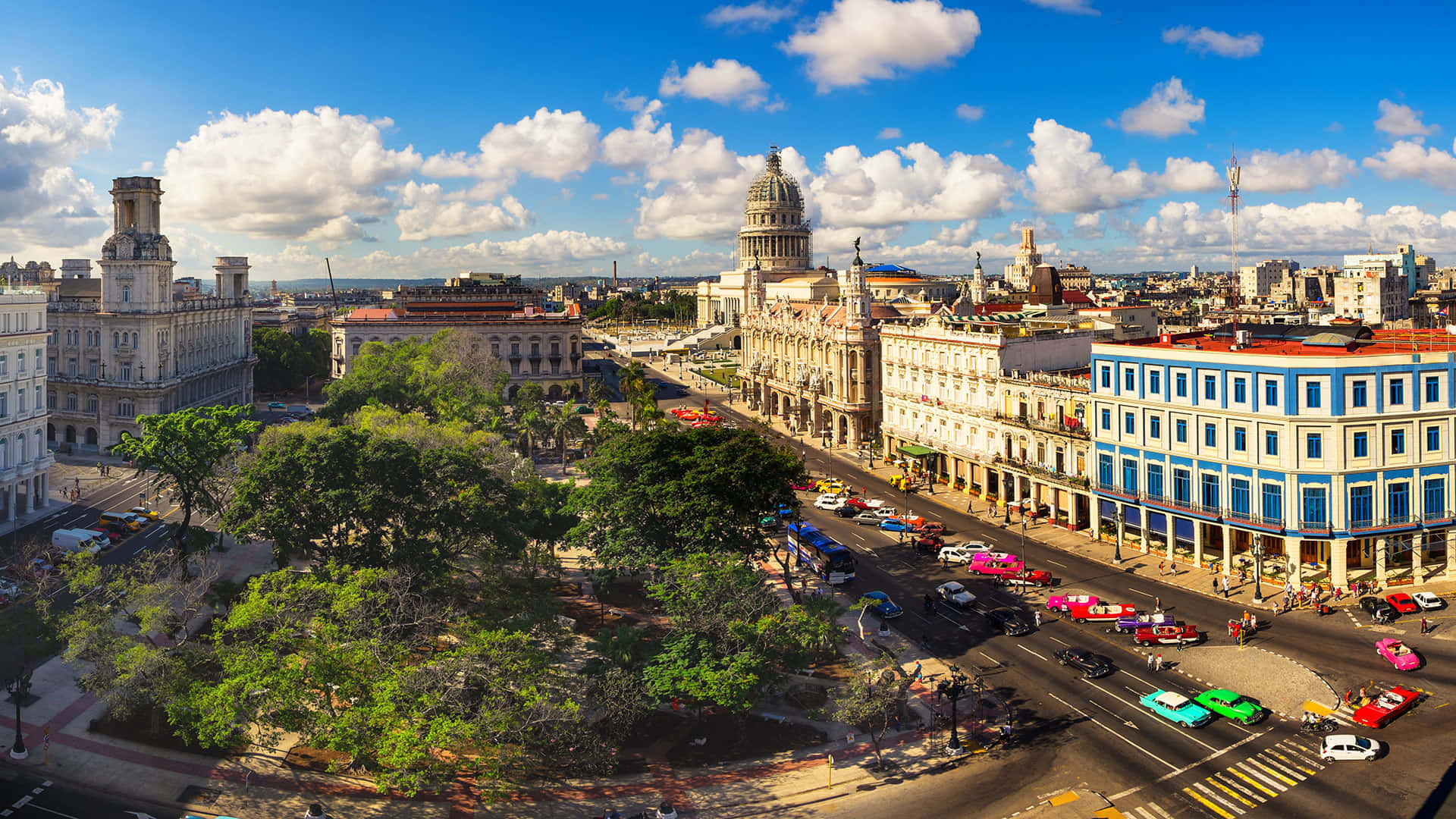 Cuba 桌布 壁紙 — 從高空俯瞰哈瓦那充滿活力的街道，兩旁是殖民時期建築和色彩繽紛的經典汽車，在晴朗的藍天和白雲下。