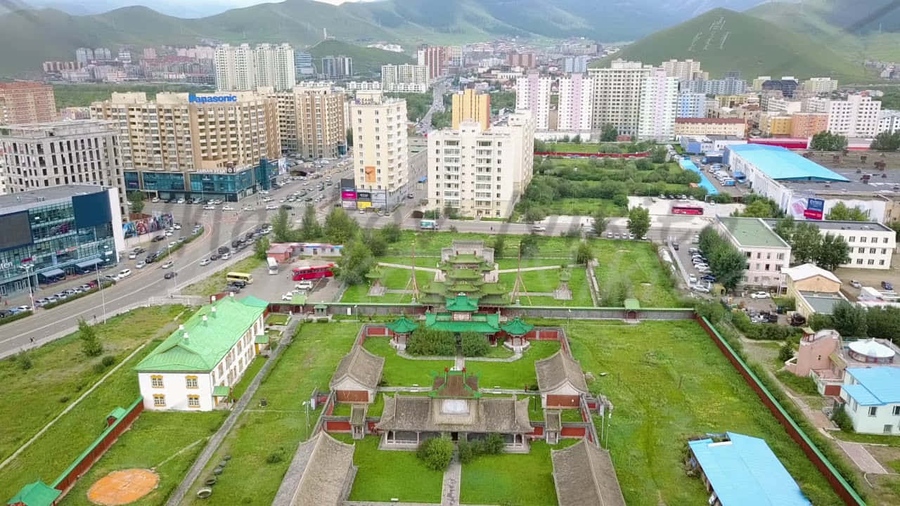 Mongolia 桌布 壁紙 — 從高空俯瞰城市景觀，現代高樓大廈與傳統綠色屋頂寺廟建築群交織，坐落於茂密的草地上。