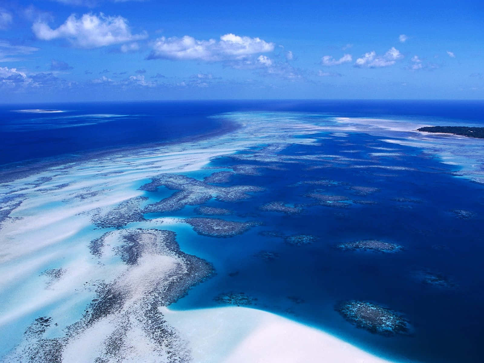 Great Barrier Reef 桌布 壁紙 — 從高空俯瞰壯麗的珊瑚礁，擁有碧綠色的潟湖和深藍色的海洋，天空明亮，雲朵稀疏。