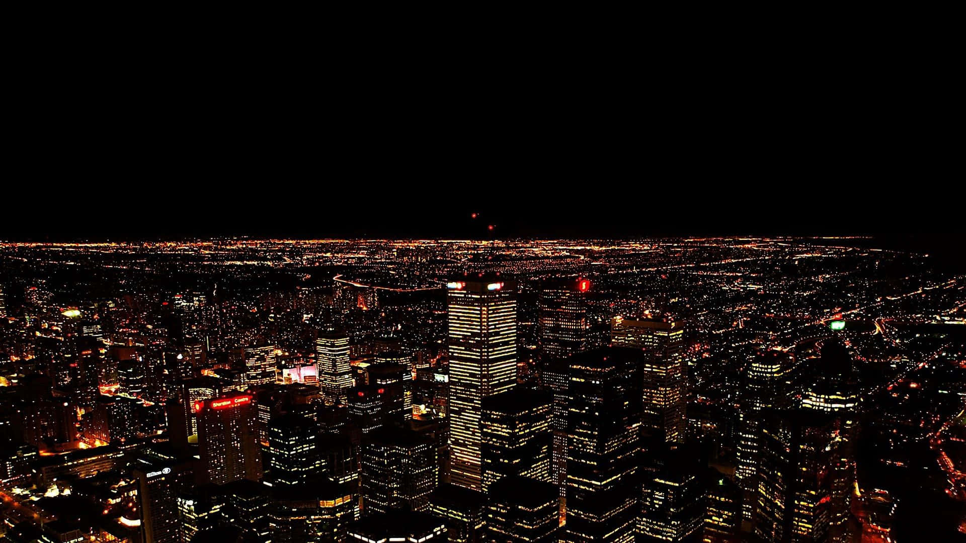 City Night 桌布 壁紙 — 從高空俯瞰夜晚中燈火通明的廣闊城市，無數發光的窗戶和街燈映襯著漆黑的天空。