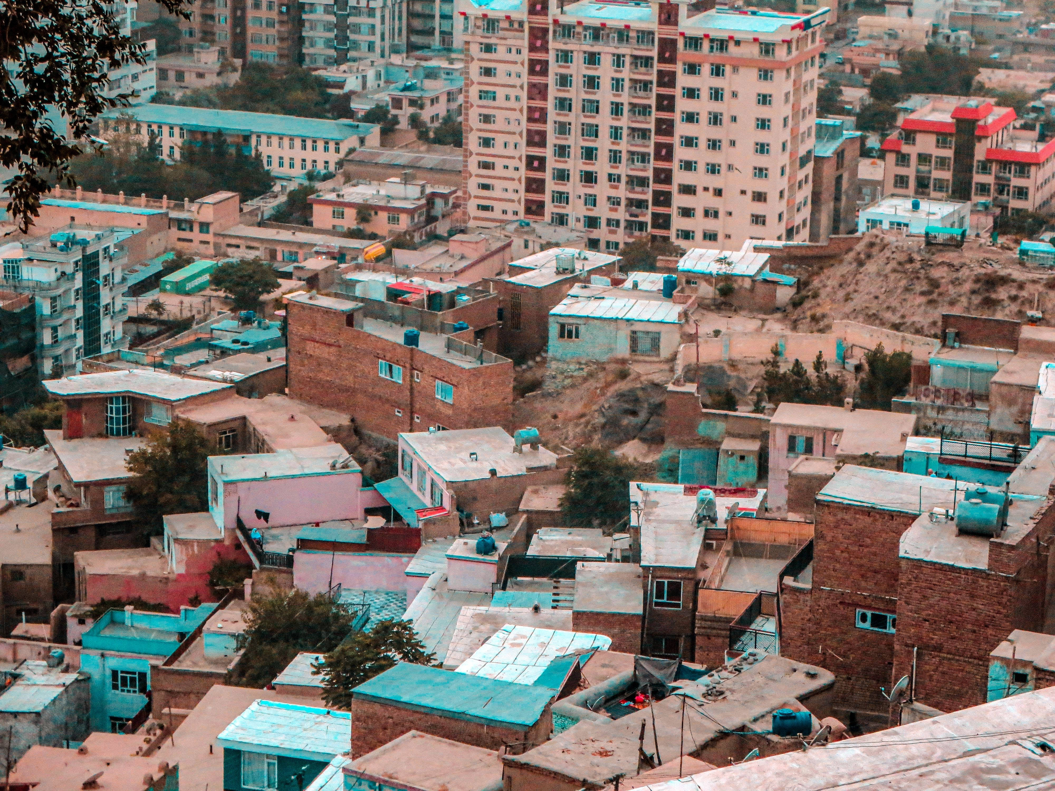 Kabul 桌布 壁紙 — 從高空俯瞰密集的城市屋頂，赤陶磚建築和充滿活力的藍綠色屋頂 nestled 在山丘之間。