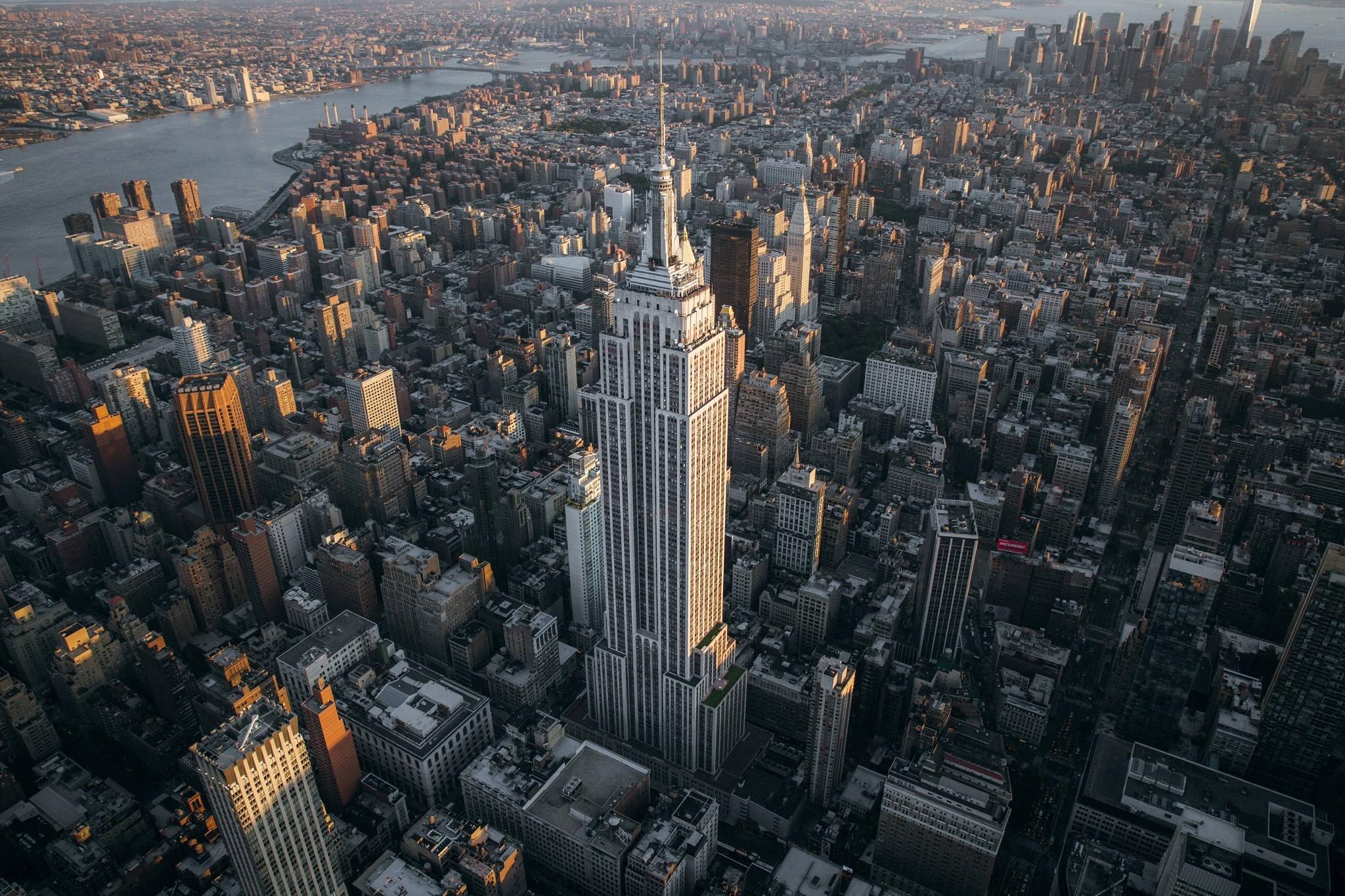empire state 桌布 壁紙 — 從高空俯瞰帝國大廈沐浴在金色夕陽光芒中，聳立於紐約市密集的城市擴展之上。