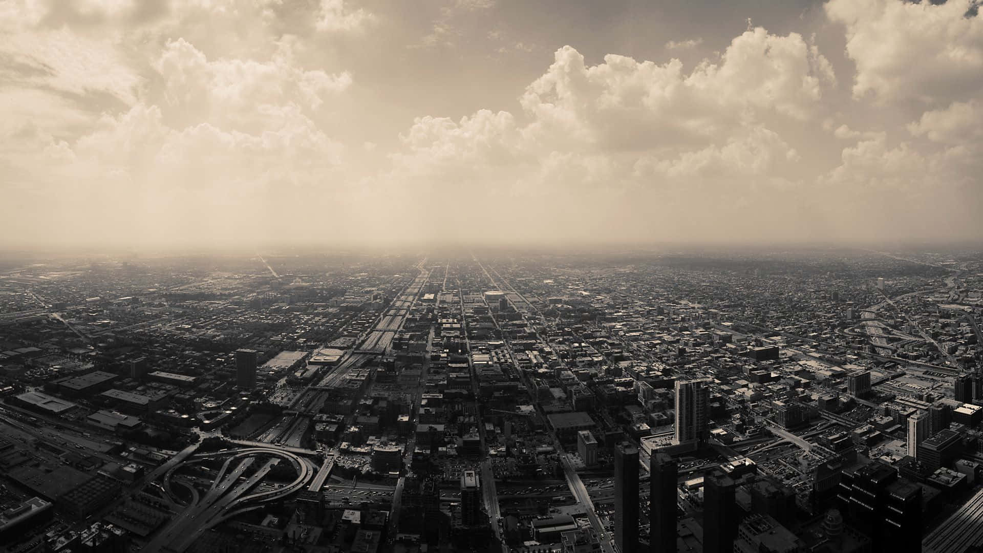 Black And White Cityscape 桌布 壁紙 — 從高空俯瞰廣闊的城市景觀，天空多雲戲劇性，帶有懷舊的棕褐色調和朦朧的陽光。