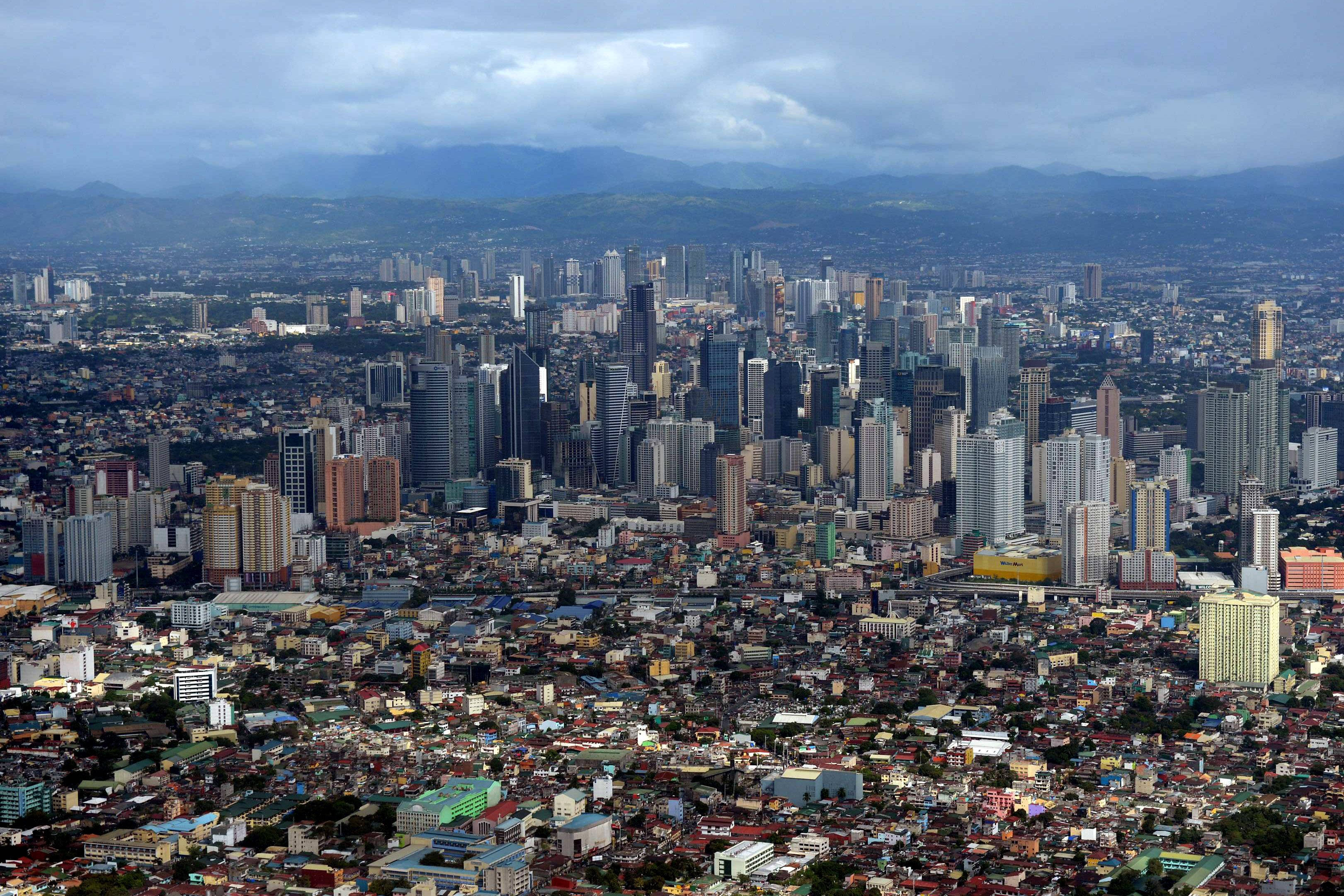 Manila 桌布 壁紙 — 從高空俯瞰廣闊的城市景觀，密集的低層住宅區過渡到現代化的高層商業區，天空多雲。