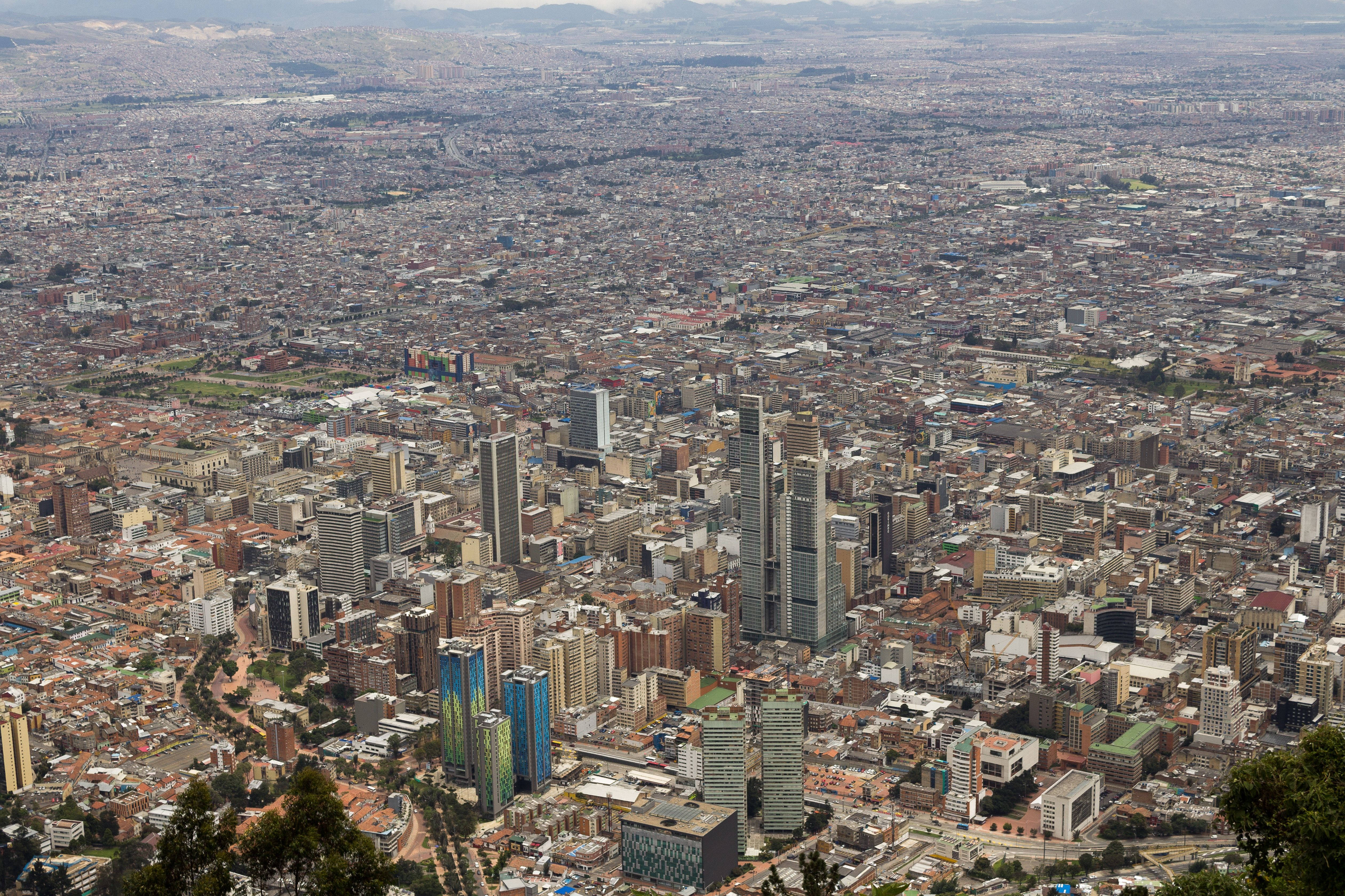Bogota 桌布 壁紙 — 從高空俯瞰廣闊的城市景觀，密集的城市網格、現代摩天大樓和遠處的山脈，在朦朧的日光下。