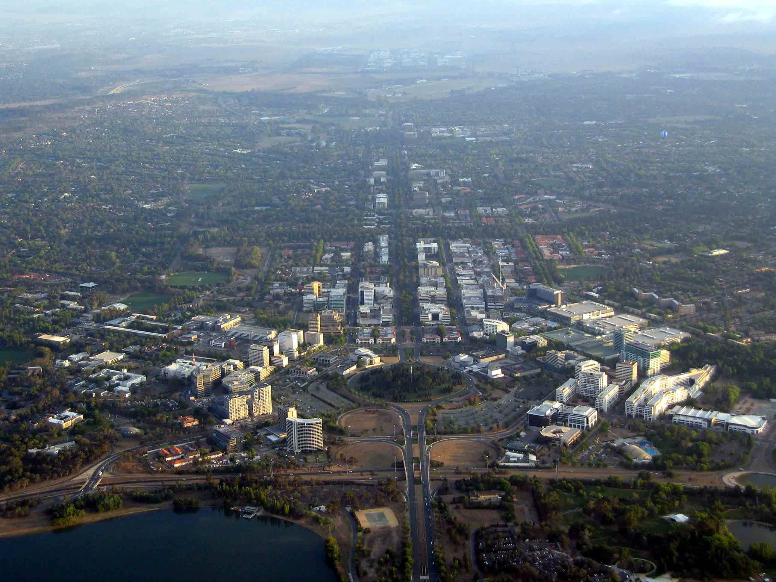 Canberra 桌布 壁紙 — 從高空俯瞰廣闊的城市景觀，擁有網格狀街道、現代建築和綠地，在朦朧的日光下。