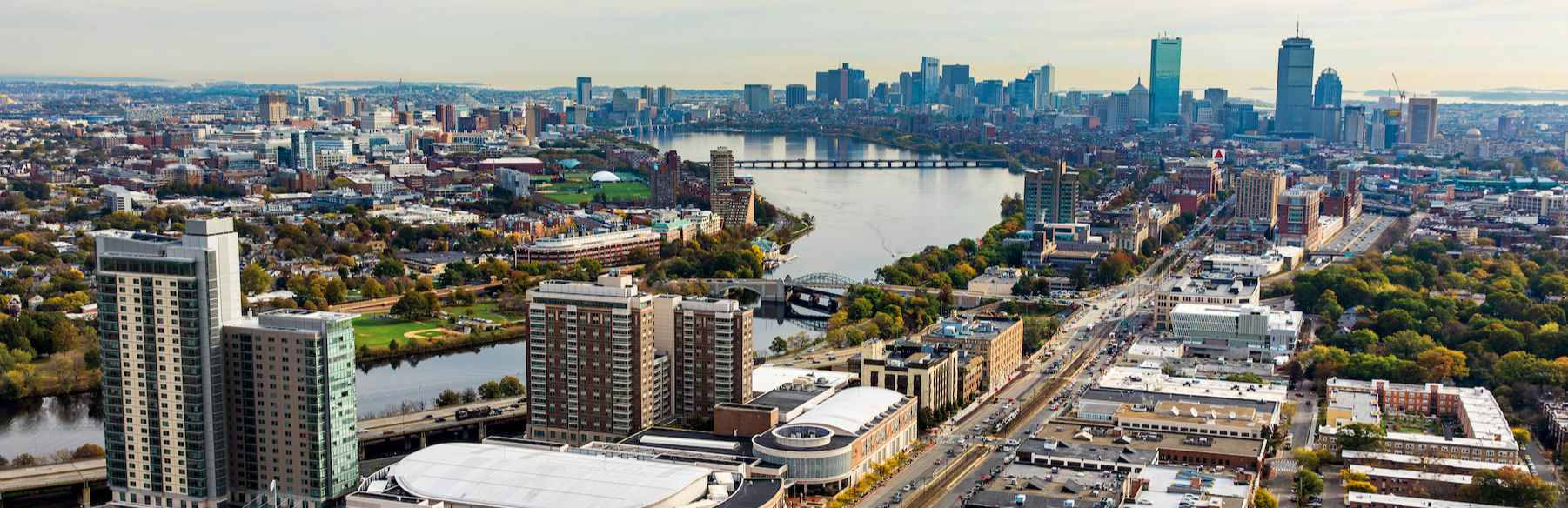 Boston 桌布 壁紙 — 從高空俯瞰廣闊的城市景觀，河流蜿蜒穿過市區，遠方天際線在朦朧天空下若隱若現。