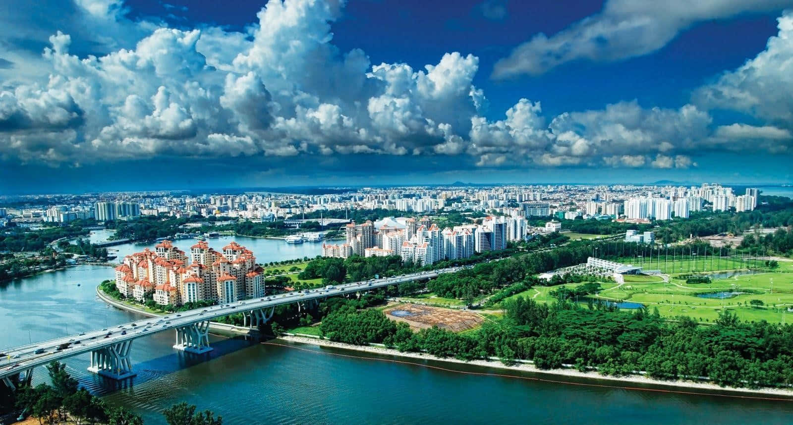Singapore 桌布 壁紙 — 從高空俯瞰廣闊的現代城市景觀，有河流橋樑、鬱鬱蔥蔥的綠色公園，以及戲劇性的藍天和蓬鬆的白雲。