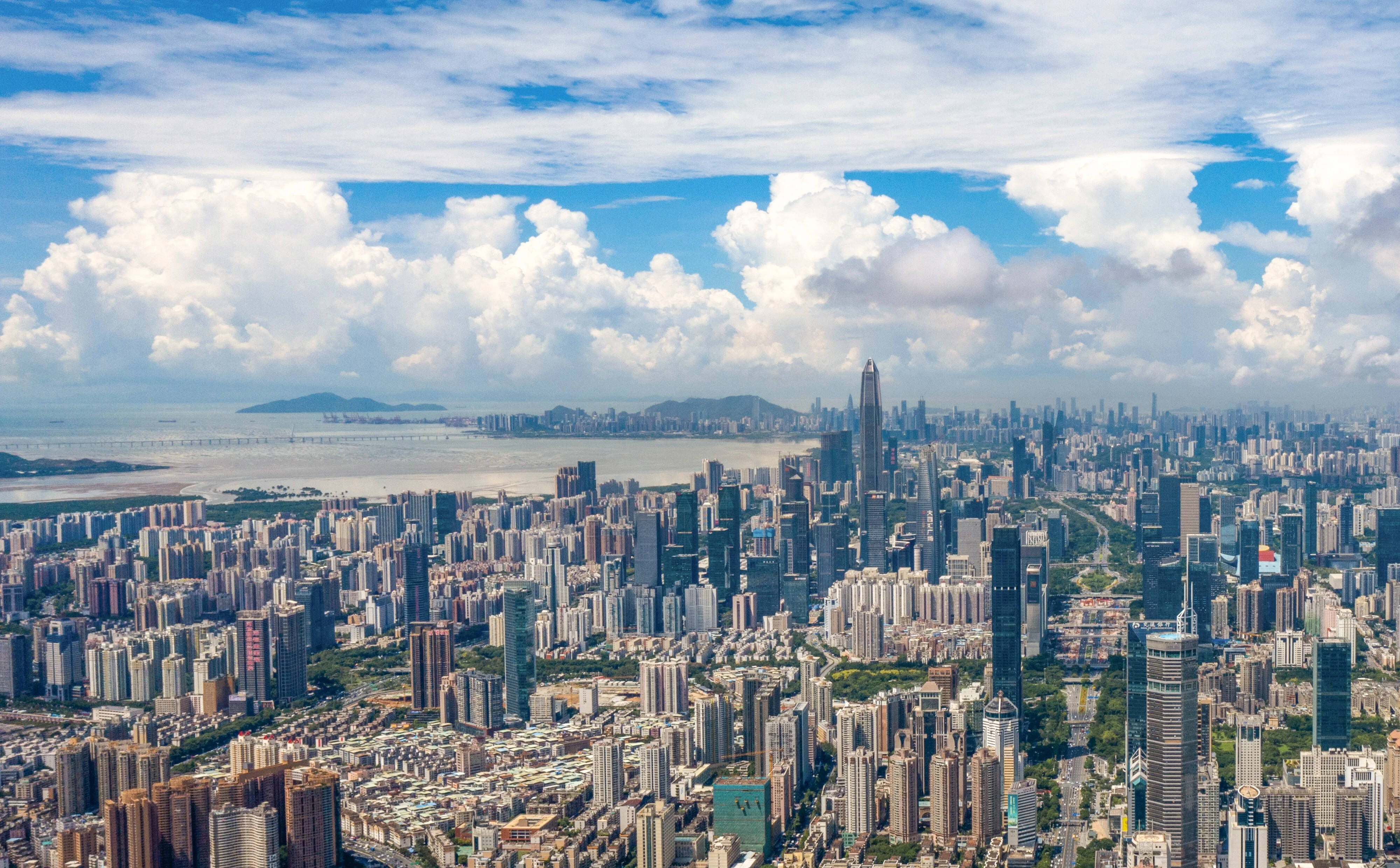 Shenzhen 桌布 壁紙 — 從高空俯瞰廣闊的現代城市景觀，藍天白雲，遠處有水。