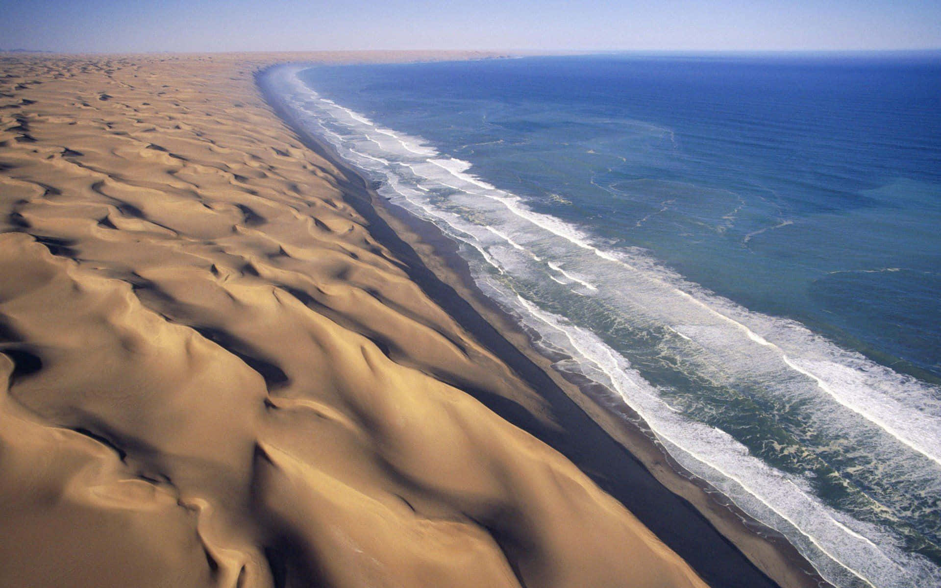 Dune 桌布 壁紙 — 從高空俯瞰廣闊的金色沙丘與碧綠的海浪在清澈藍天下交匯。