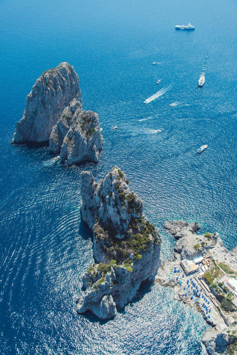 Capri 桌布 壁紙 — 從高空俯瞰戲劇性的岩石島嶼從充滿活力的藍色海洋中突出，下方有船隻和沿海城鎮。