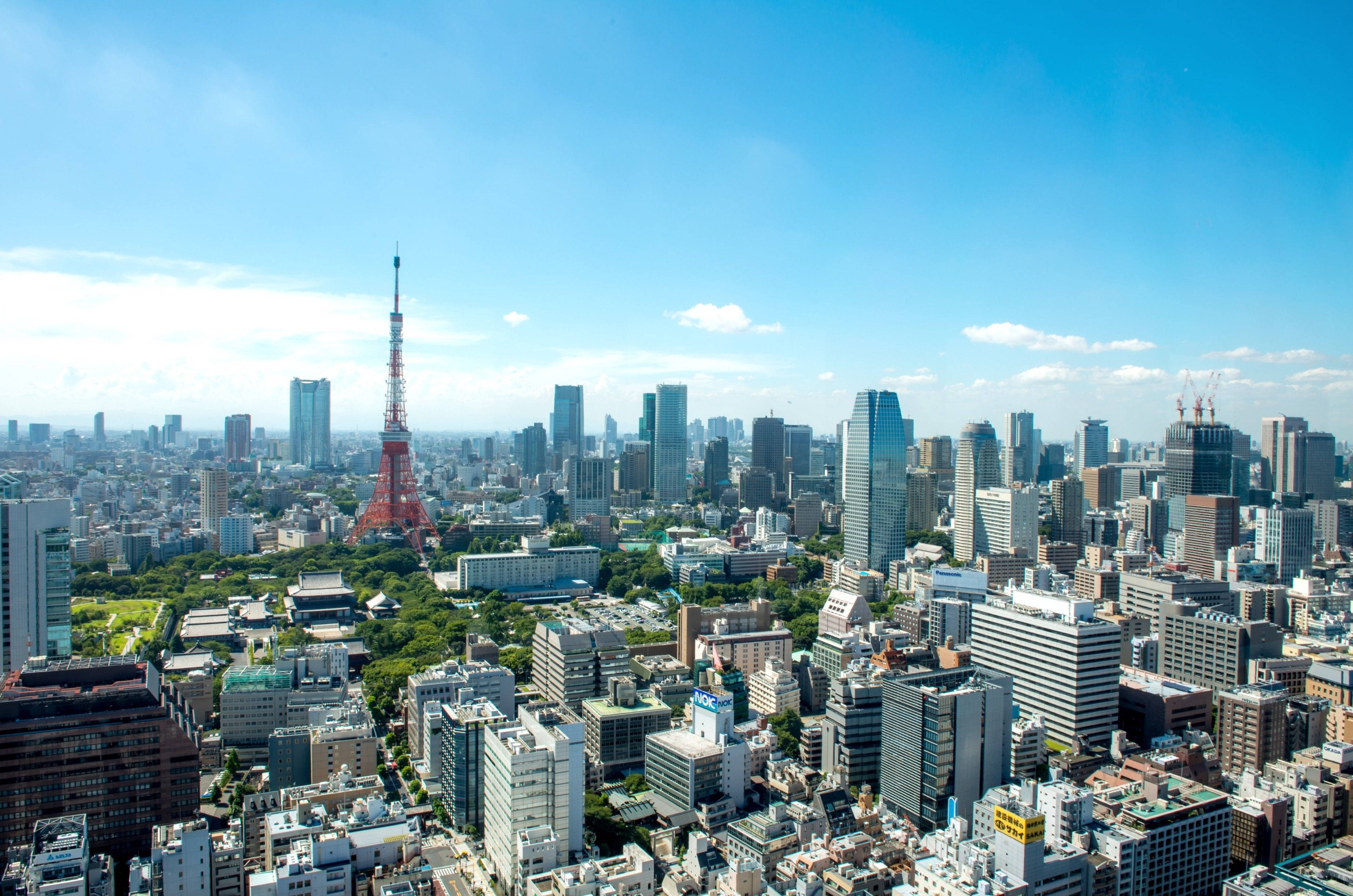 東京 桌布 壁紙 — 從高空俯瞰東京天際線，紅色東京塔在密集的城市建築上方聳立，藍天白雲清晰可見。