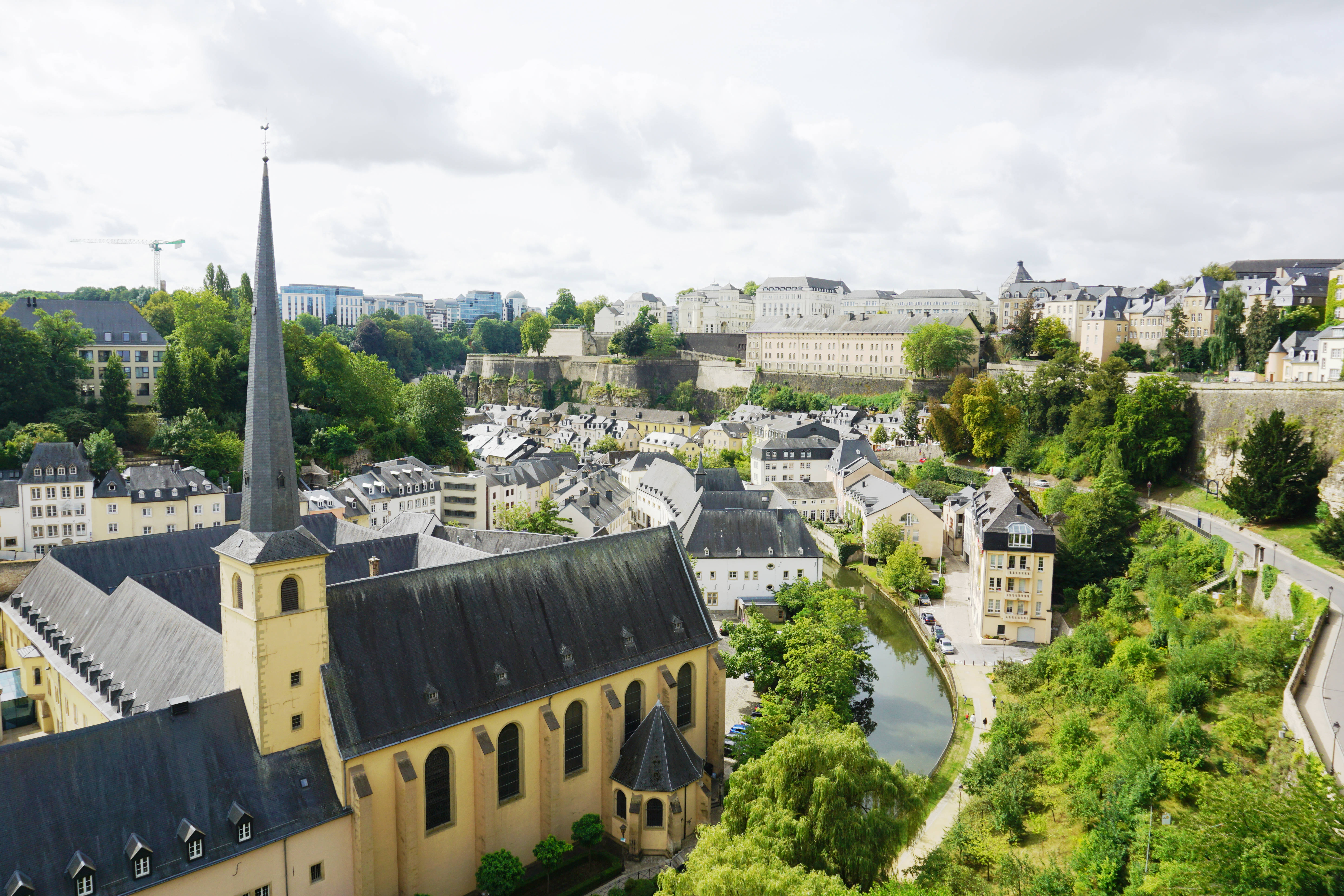 Luxembourg 桌布 壁紙 — 從高空俯瞰歷史悠久的歐洲城市，擁有突出的教堂尖頂、蜿蜒的河流和茂密的綠植，天空多雲。