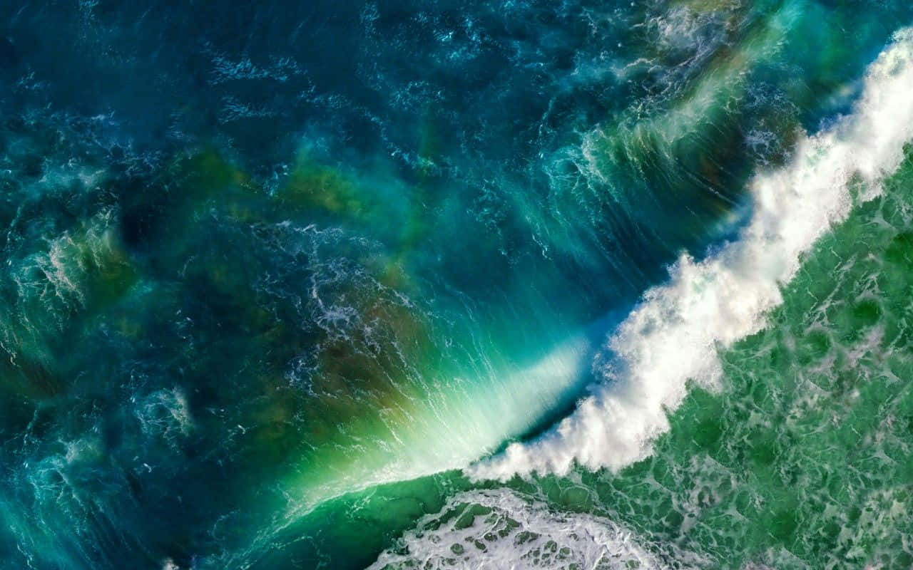 Ocean Waves 桌布 壁紙 — 從高空俯瞰洶湧的海浪拍打著白色泡沫，撞擊在充滿活力的藍綠色和綠色海面上。