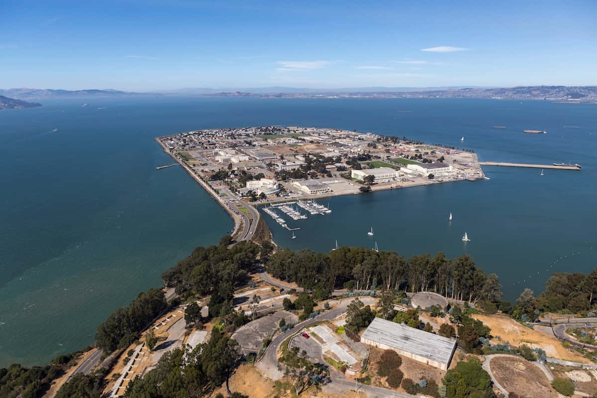 California Island 桌布 壁紙 — 從高空俯瞰海岸島嶼小鎮，碼頭、帆船和蜿蜒穿過綠色山丘的道路，在清澈的藍天下。