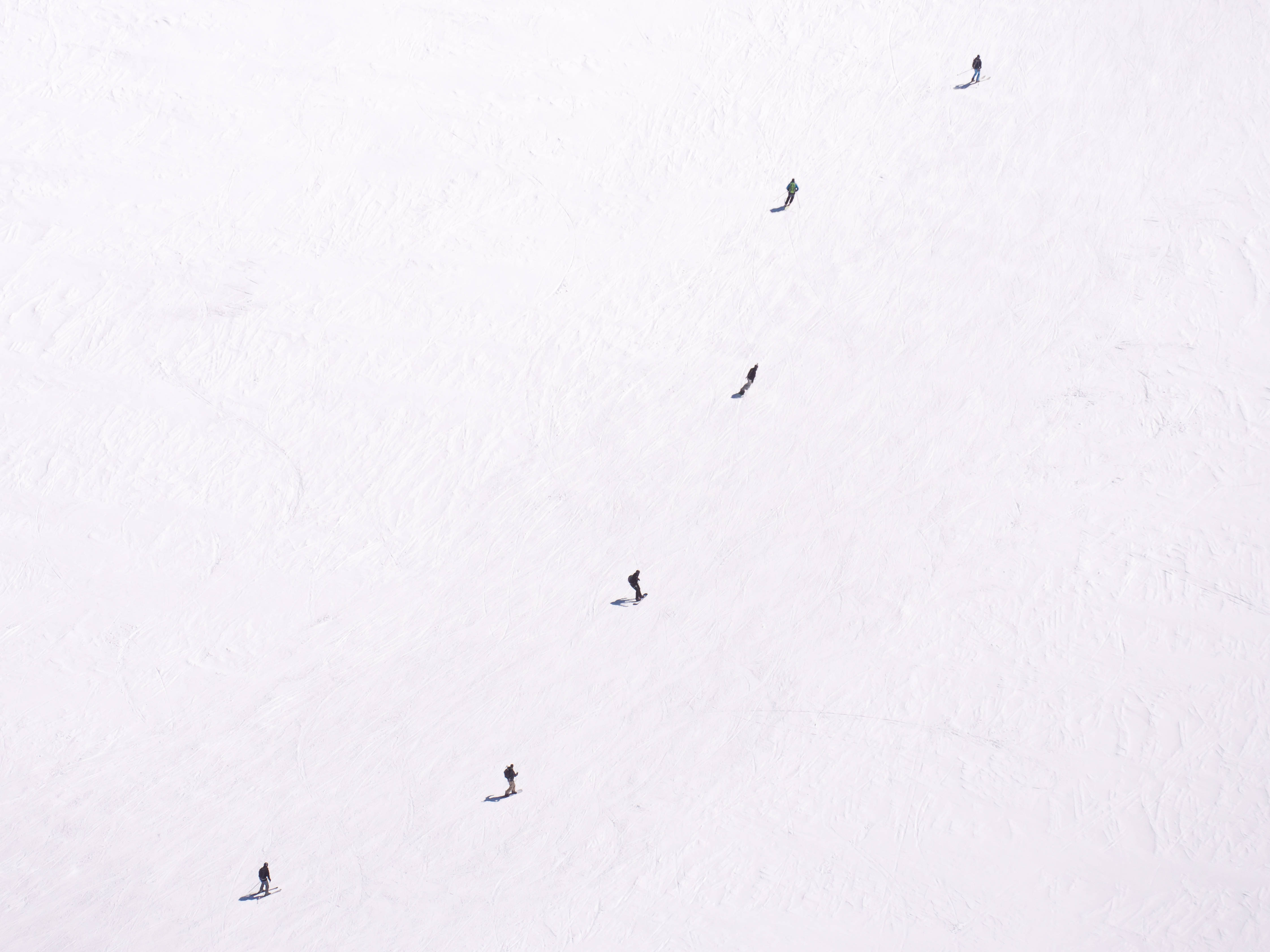 off white 桌布 壁紙 — 從高空俯瞰滑雪板運動員在廣闊雪坡上滑下，留下平行軌跡。