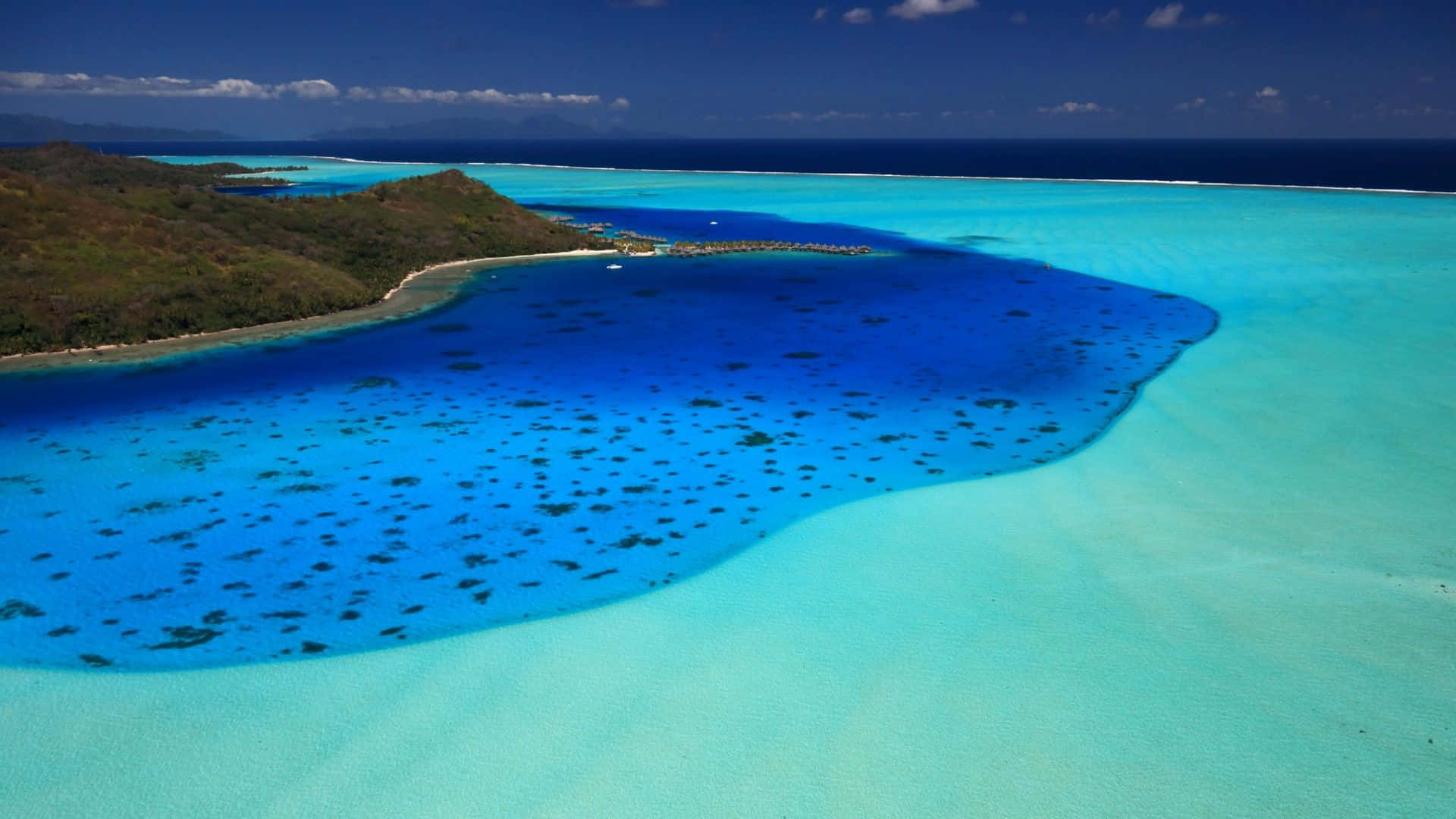 Bora Bora 桌布 壁紙 — 從高空俯瞰熱帶環礁，碧綠潟湖被茂密綠島環繞，天空清澈湛藍。