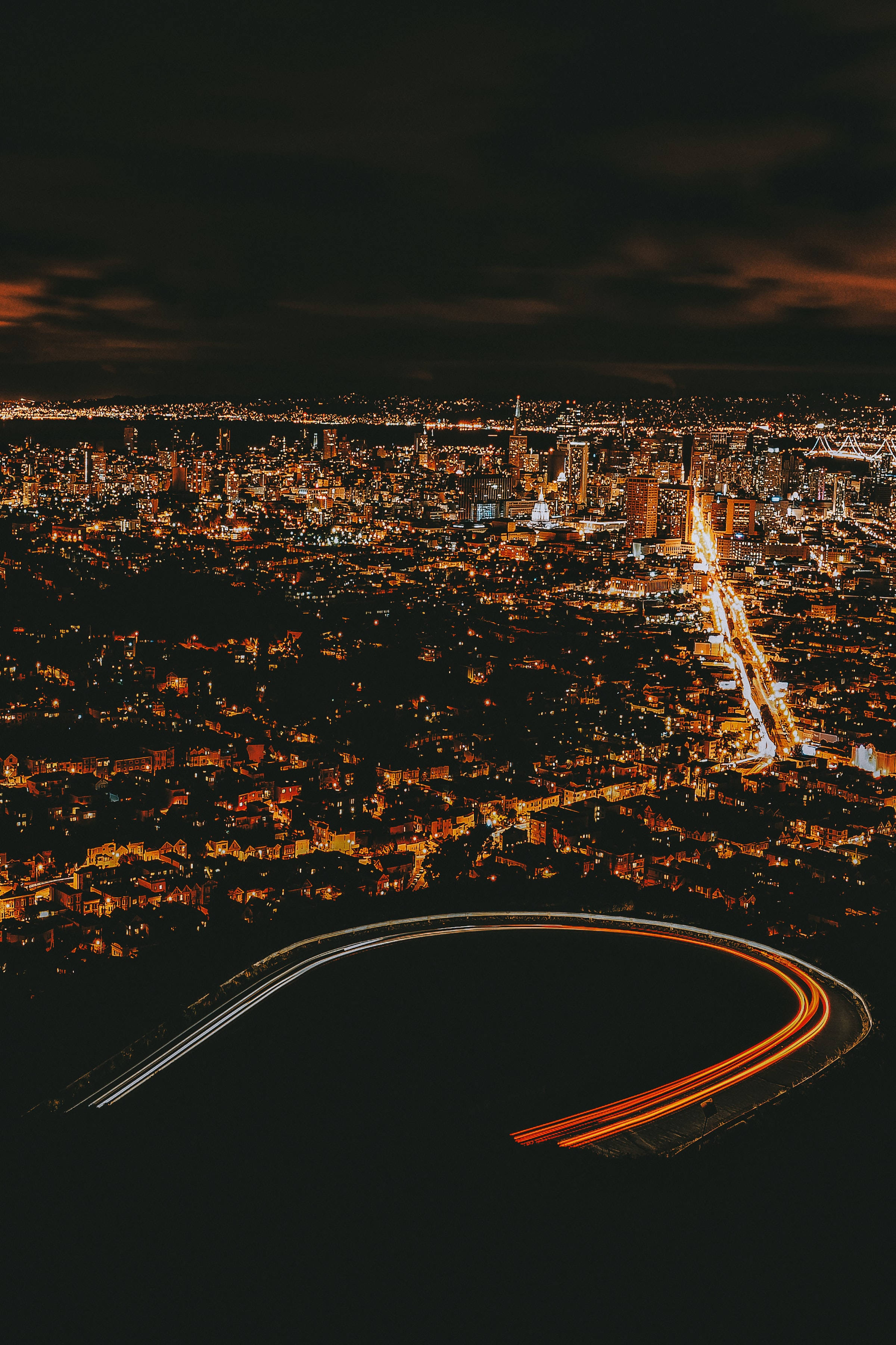 夜空 桌布 壁紙 — 從高空俯瞰的夜景，展現廣闊的城市景觀，燈光閃爍，長曝光下形成彎曲的高速公路線條。