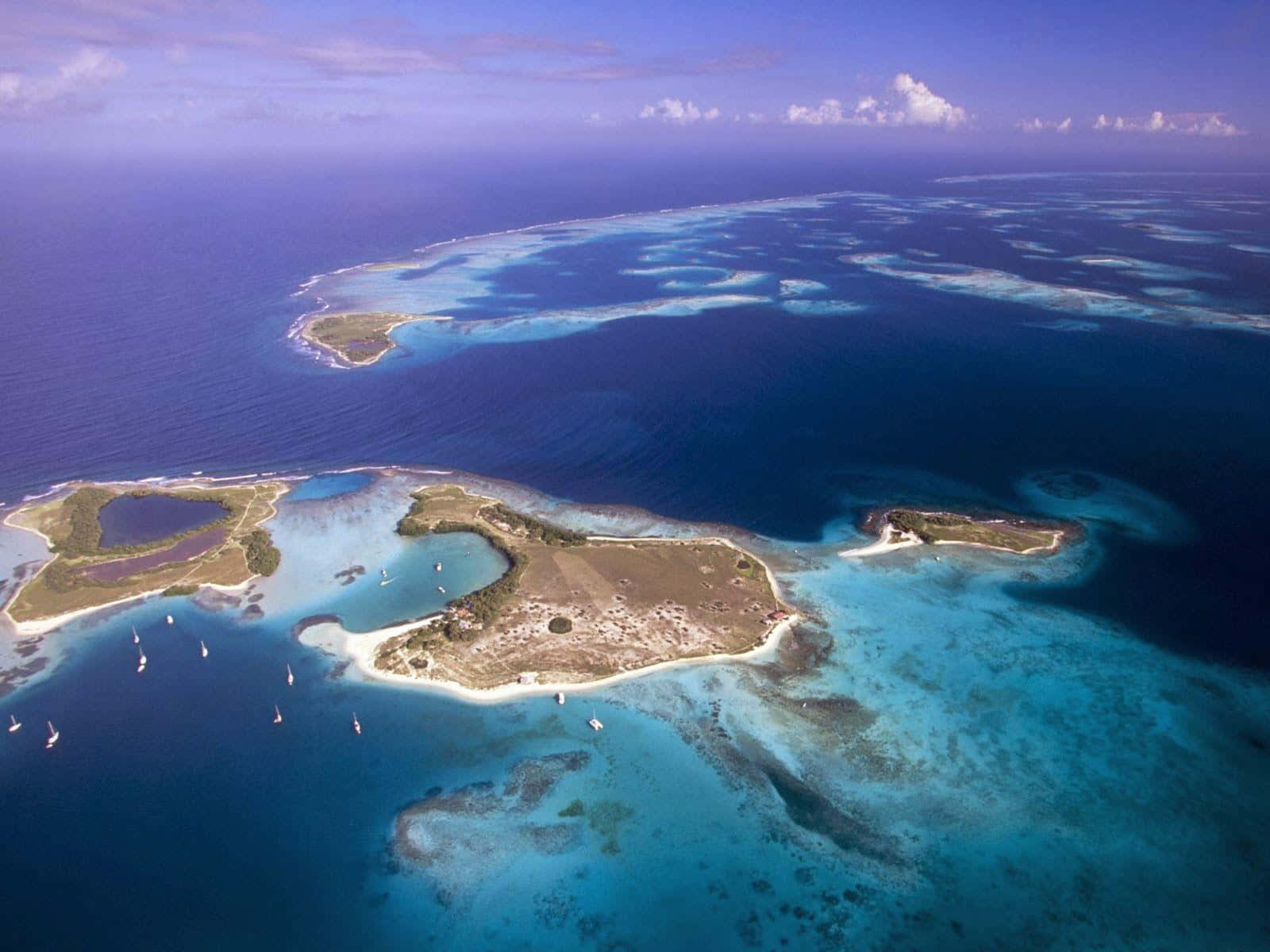 Bermuda Triangle 桌布 壁紙 — 從高空俯瞰碧綠潟湖島嶼，擁有白色沙灘和散落的帆船，在清澈的藍天下。