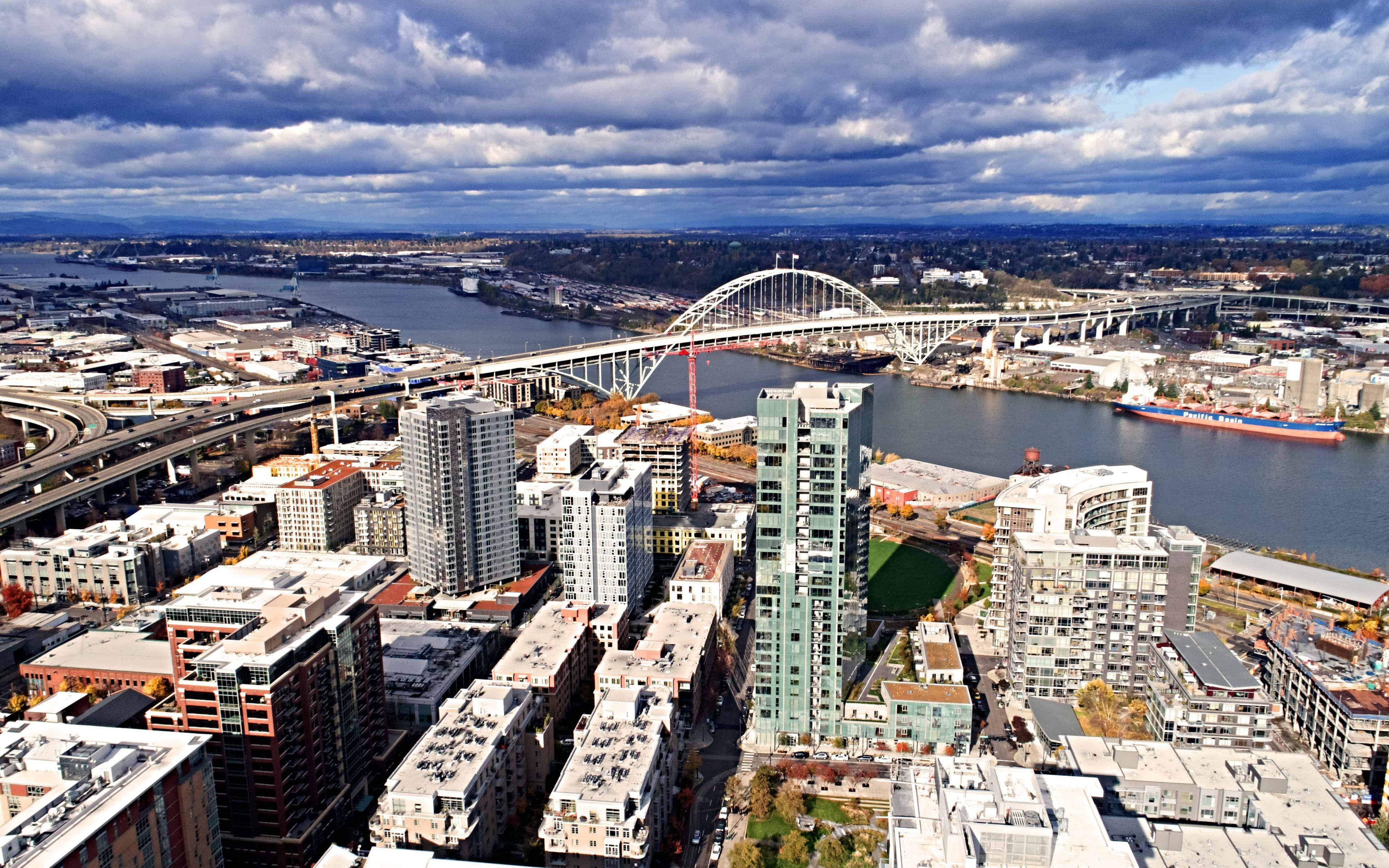 Portland 桌布 壁紙 — 從高空俯瞰繁忙的城市景觀，一座突出的拱橋橫跨寬闊的河流，天空烏雲密佈，氣氛戲劇化。