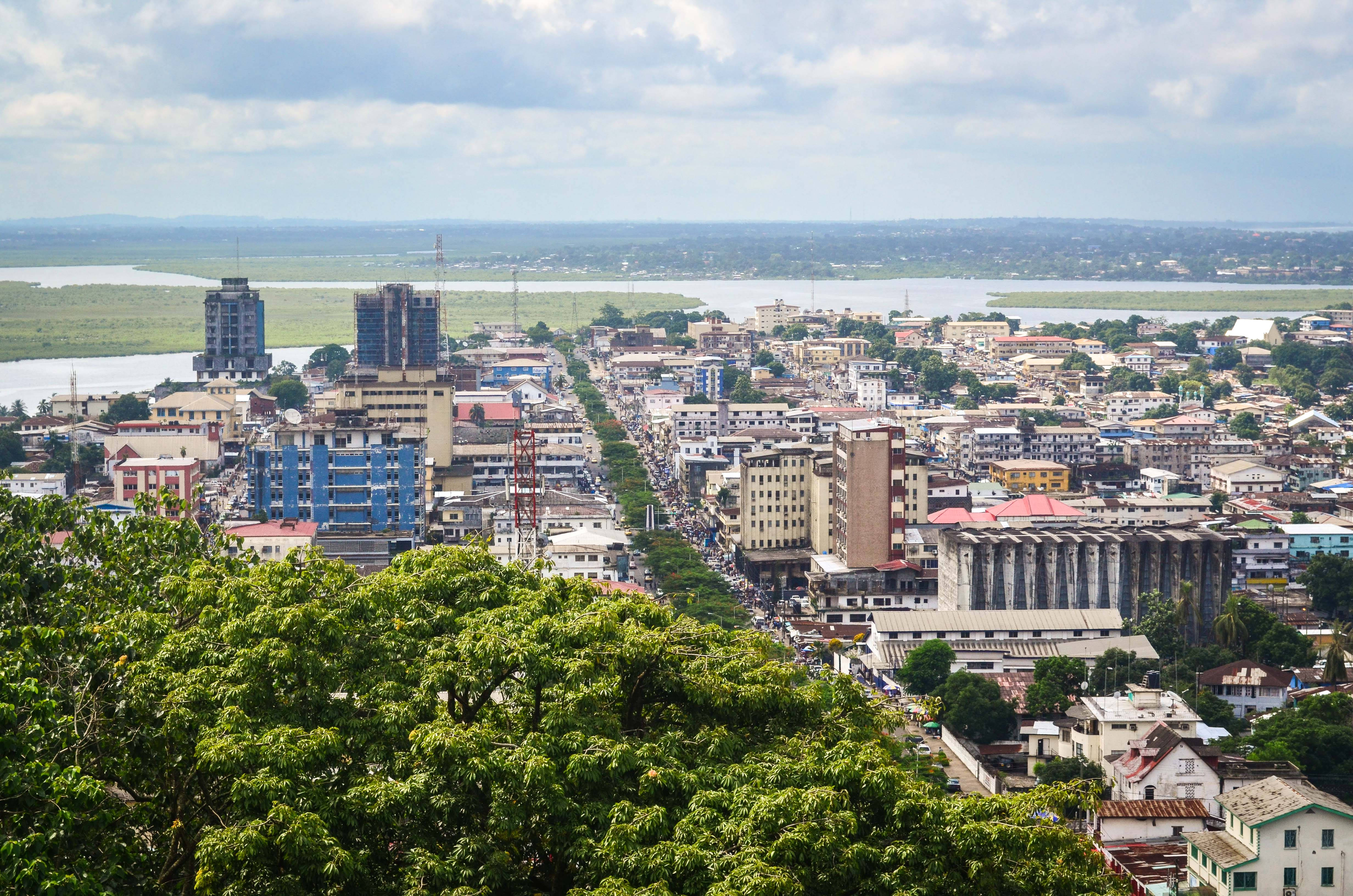 Liberia 桌布 壁紙 — 從高空俯瞰繁忙的城市景觀，密集的建築物、寬闊的河流，以及部分多雲天空下茂密的綠樹。