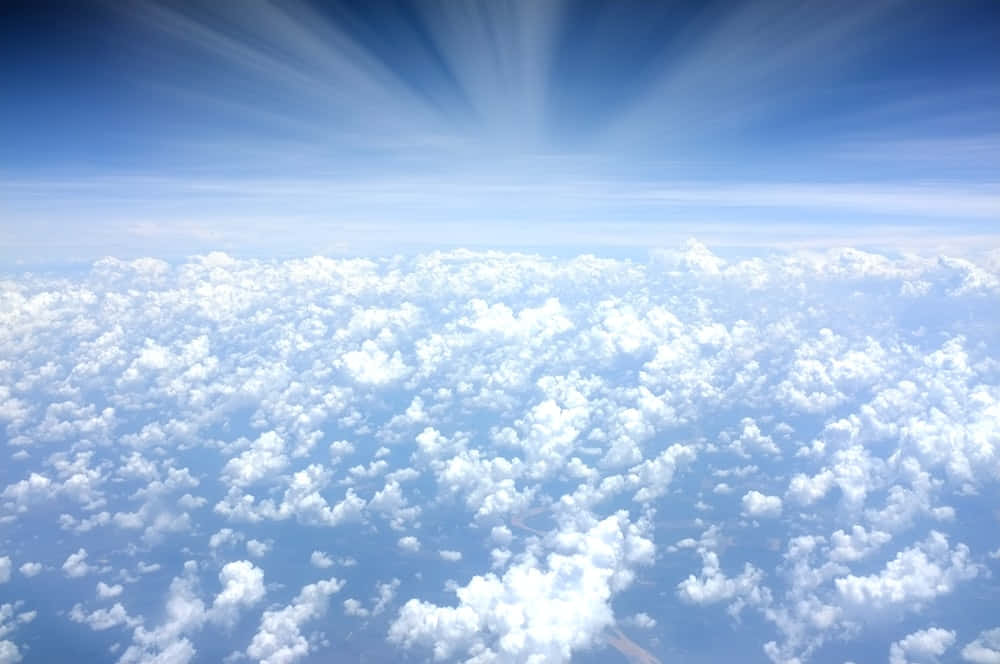 Beautiful Heaven 桌布 壁紙 — 從高空俯瞰蓬鬆的白雲在燦爛的藍天下延伸，陽光從上方迸發而出。
