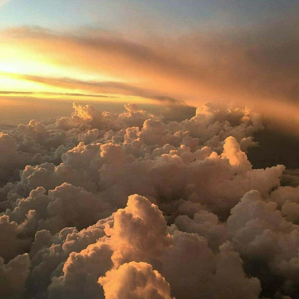 美學雲朵 桌布 壁紙 — 從高空俯瞰蓬鬆的雲朵沐浴在金色日落光芒中，上方是柔和的橙色和藍色天空。