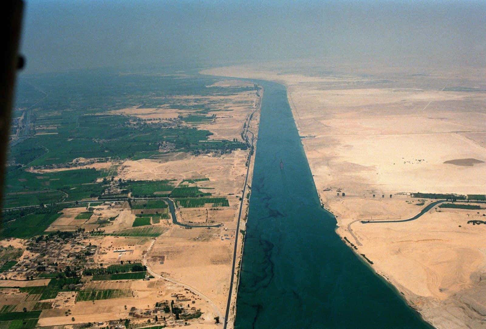 Cargo Ship 桌布 壁紙 — 從高空俯瞰蘇伊士運河在朦朧天空下穿過沙漠和農田的景象。