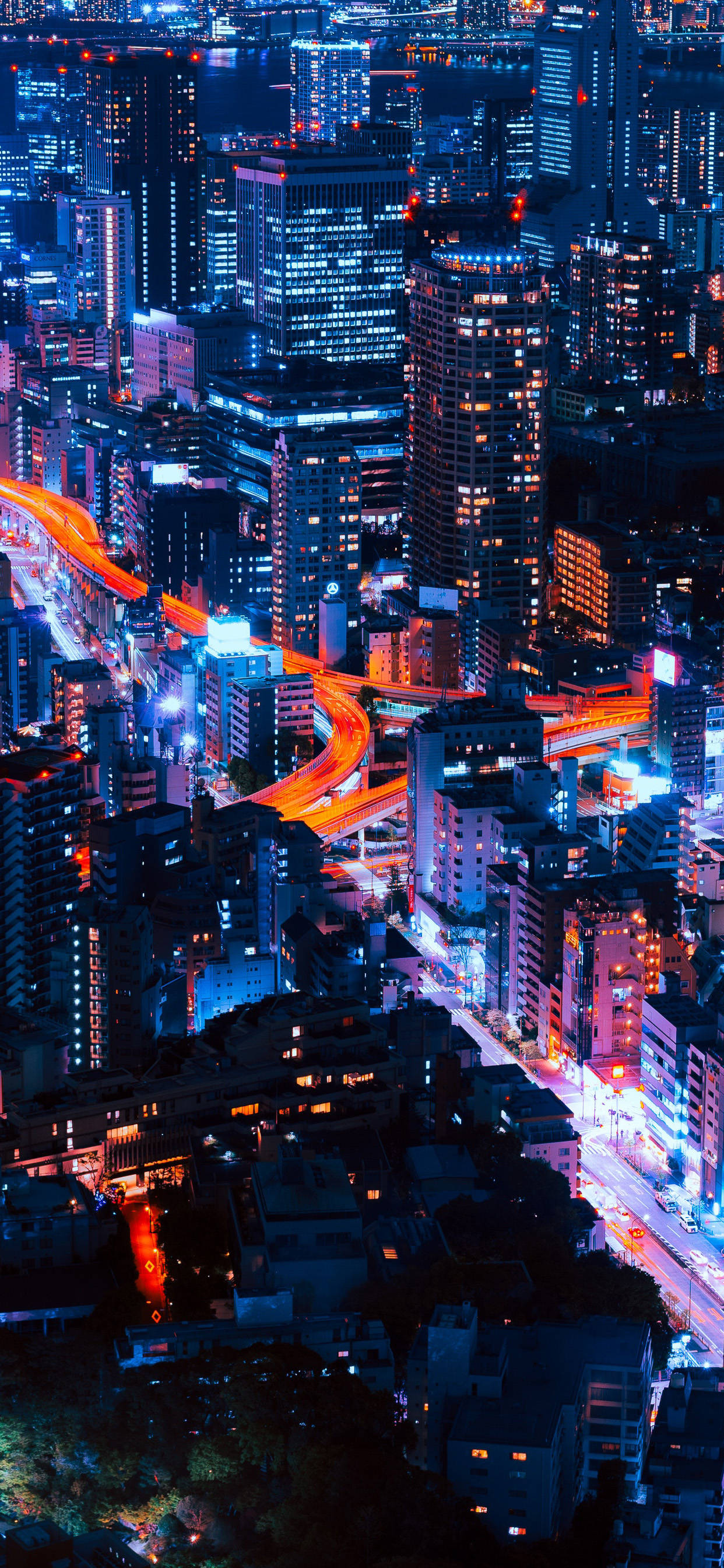 攝影 桌布 壁紙 — 從高空俯瞰霓虹燈照亮嘅城市夜景，發光嘅橙色高速公路蜿蜒穿過高聳嘅摩天大樓。