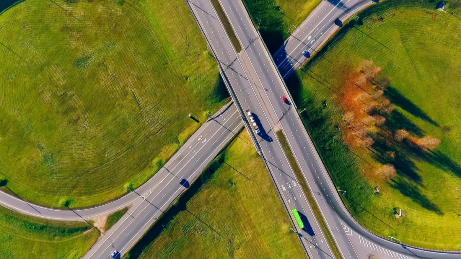 Highways 桌布 壁紙 — 從高空俯瞰高速公路交匯處穿過充滿活力的綠色起伏山丘，散落著秋天的樹木和行駛中的車輛。