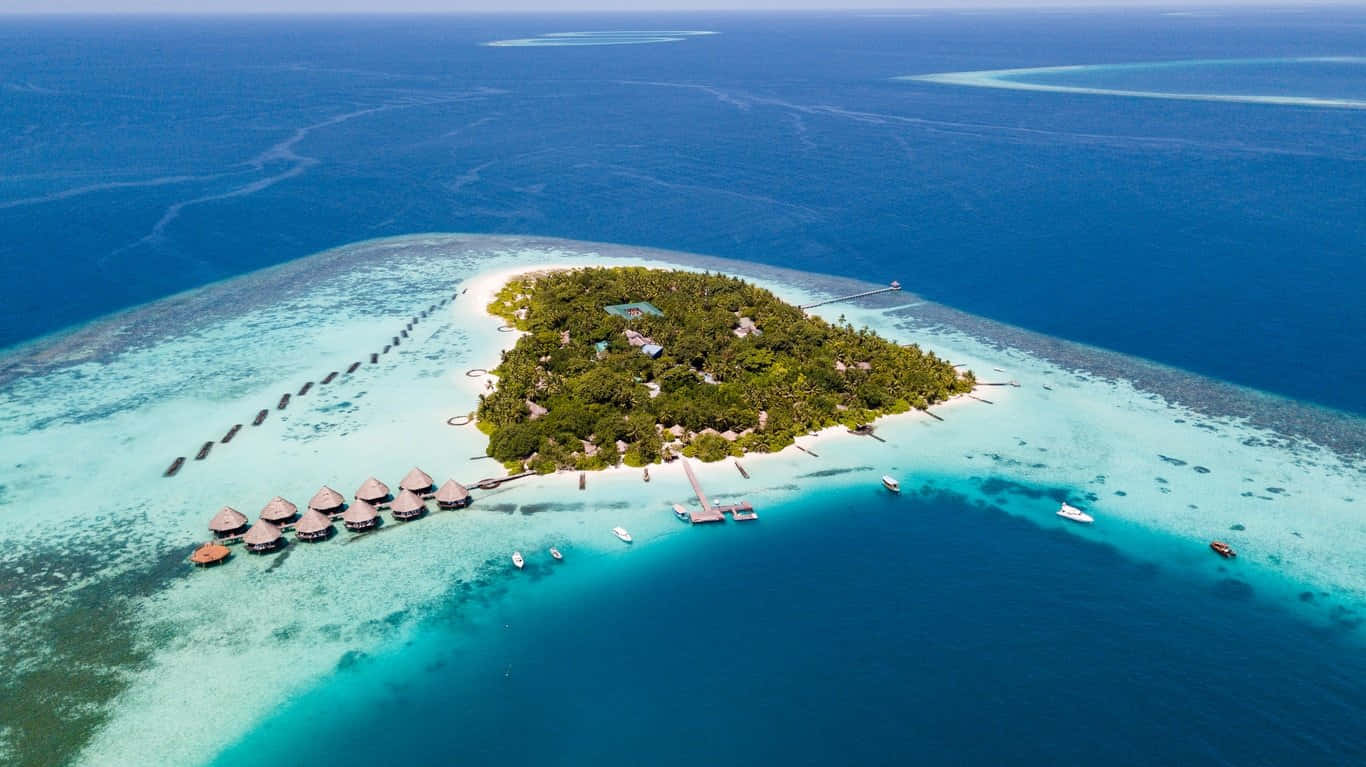 Maldives Island 桌布 壁紙 — 從高空俯瞰鬱鬱蔥蔥的熱帶島嶼，擁有水上平房和碧綠潟湖，四周環繞著深藍色海洋。