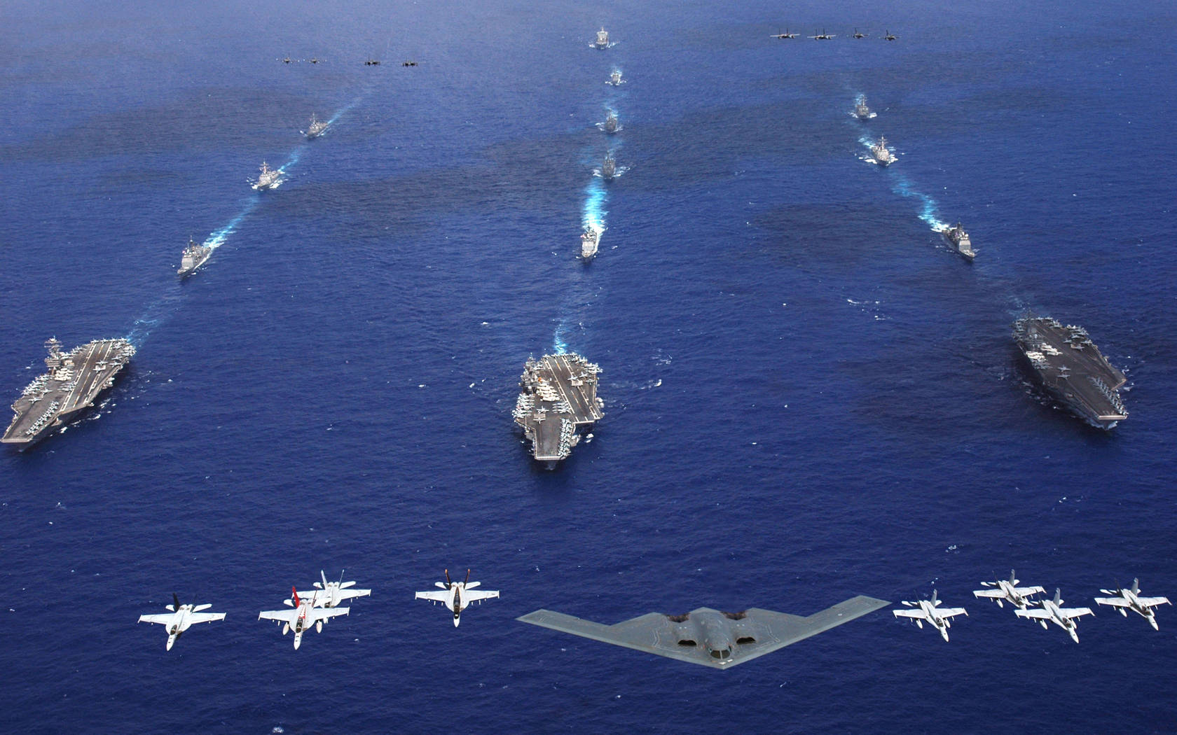 Warship 桌布 壁紙 — 從高空俯瞰龐大艦隊，包括航空母艦和戰鬥機在深藍色海洋上空編隊飛行。