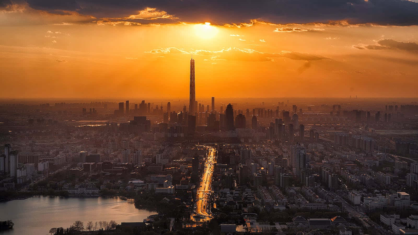 Cute Sunset 桌布 壁紙 — 從高聳摩天大樓背後散發出金色光芒的廣闊城市景觀的空中日落景觀。