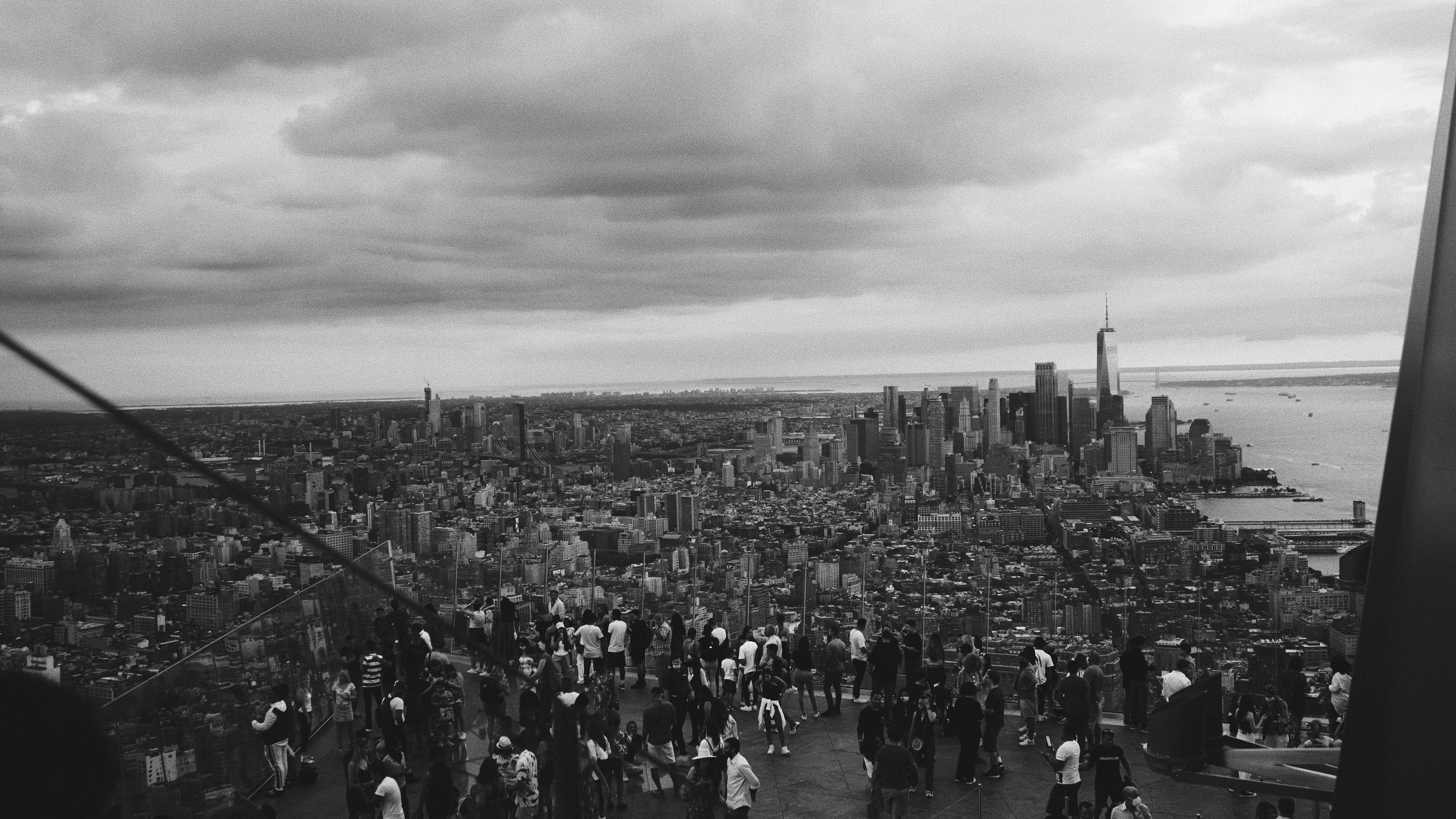 Nyc Aesthetic 桌布 壁紙 — 從高處俯瞰紐約市天際線的黑白全景，下方人群湧動，天空多雲。
