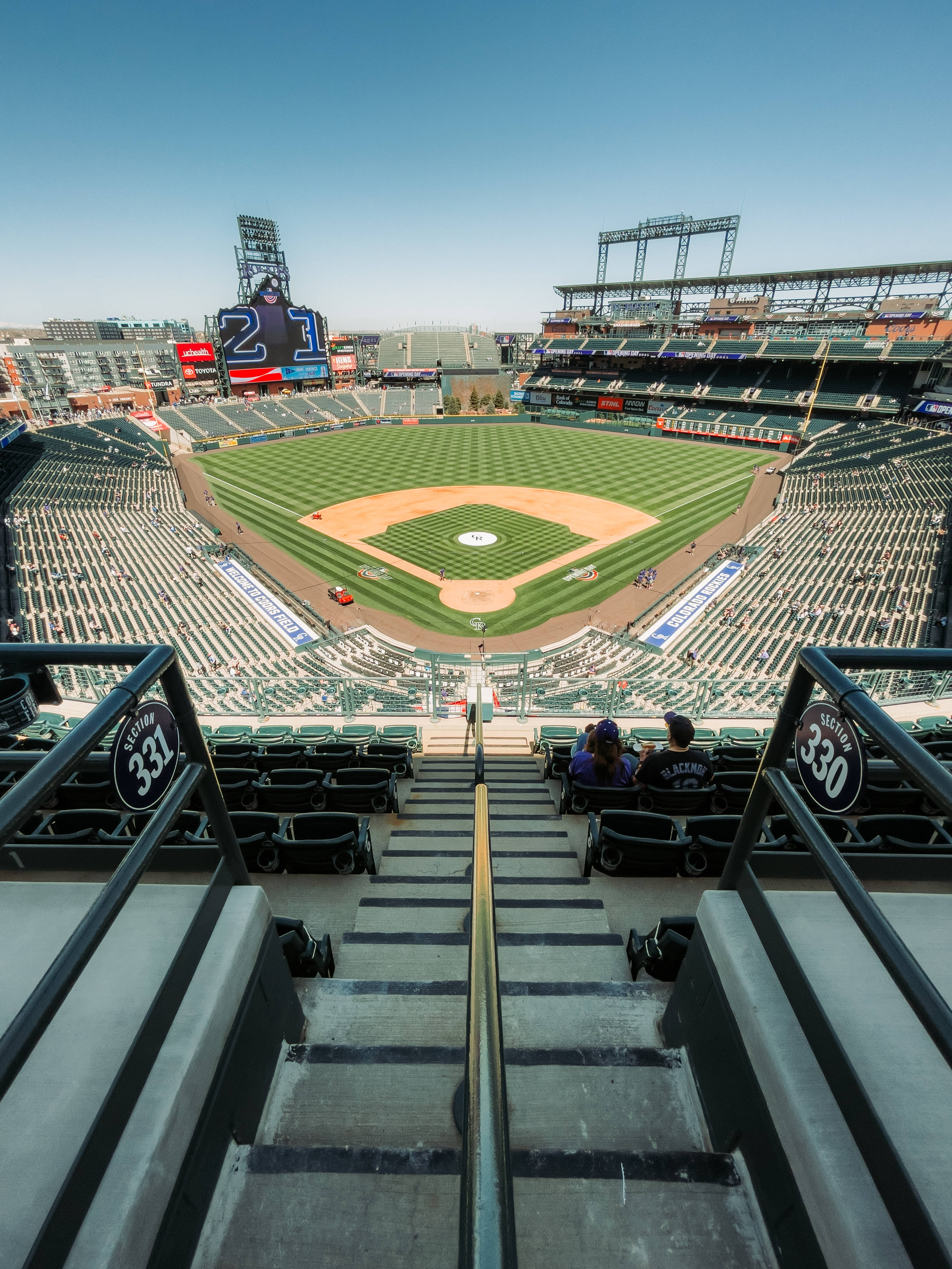 MLB 桌布 壁紙 — 從高角度俯瞰一個陽光普照的棒球場，空座位和充滿活力的綠色球場在清澈的藍天下。