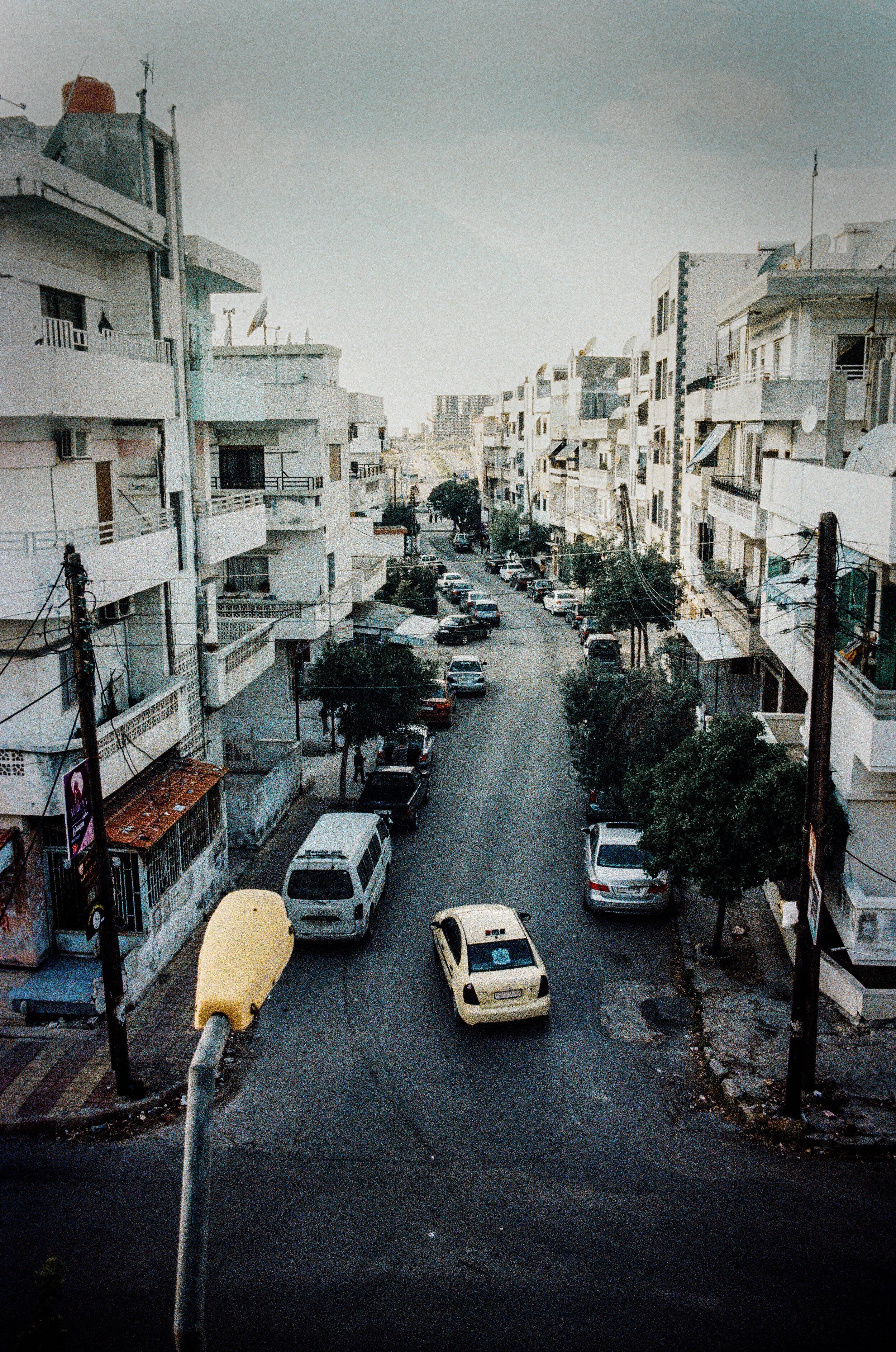 Syria 桌布 壁紙 — 從高角度俯瞰一條狹窄的城市街道，兩旁是白色公寓樓和停放的汽車，天空多雲。